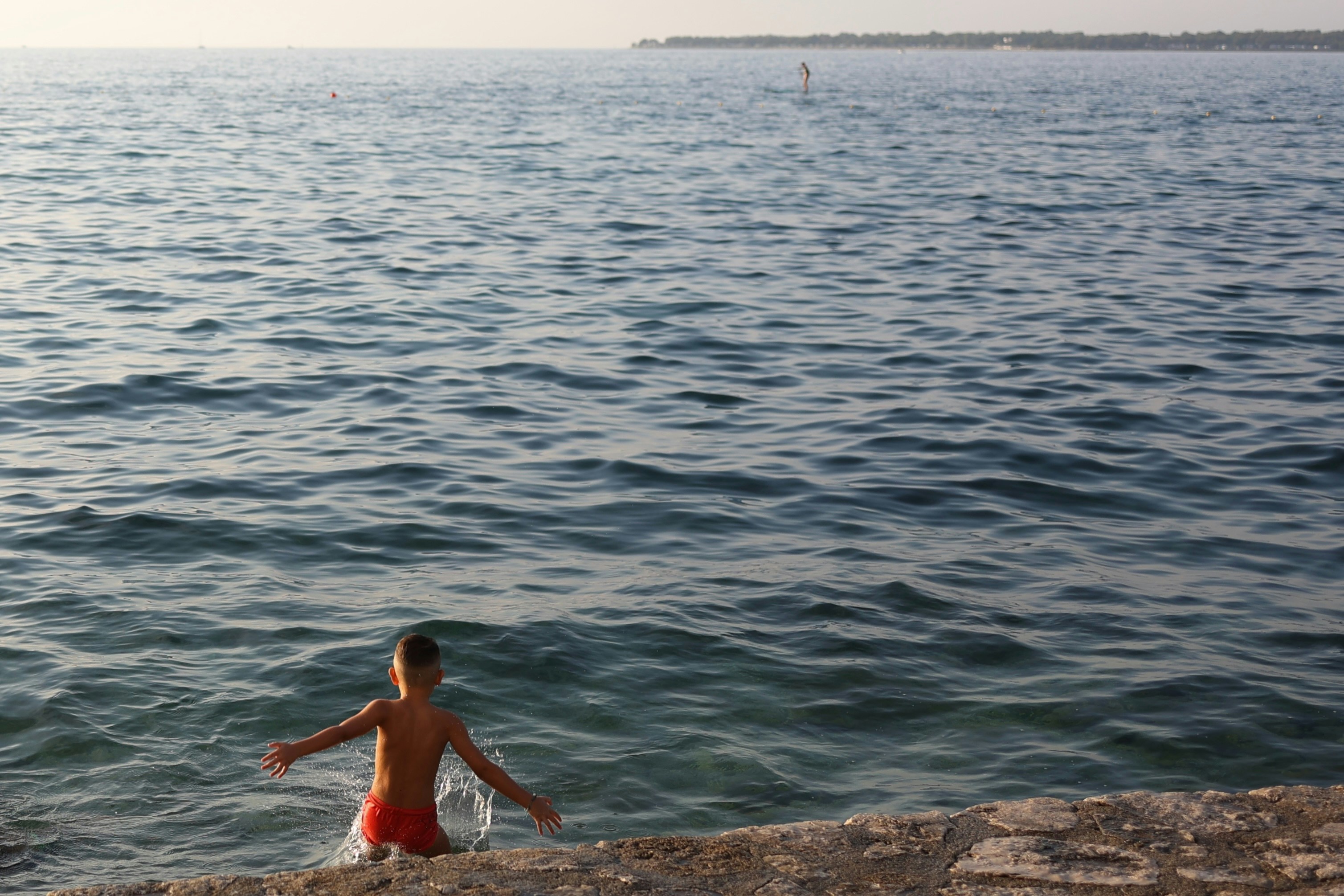 Un ragazzo in un costume da bagno rosso in piedi sul bordo di una scogliera vicino al