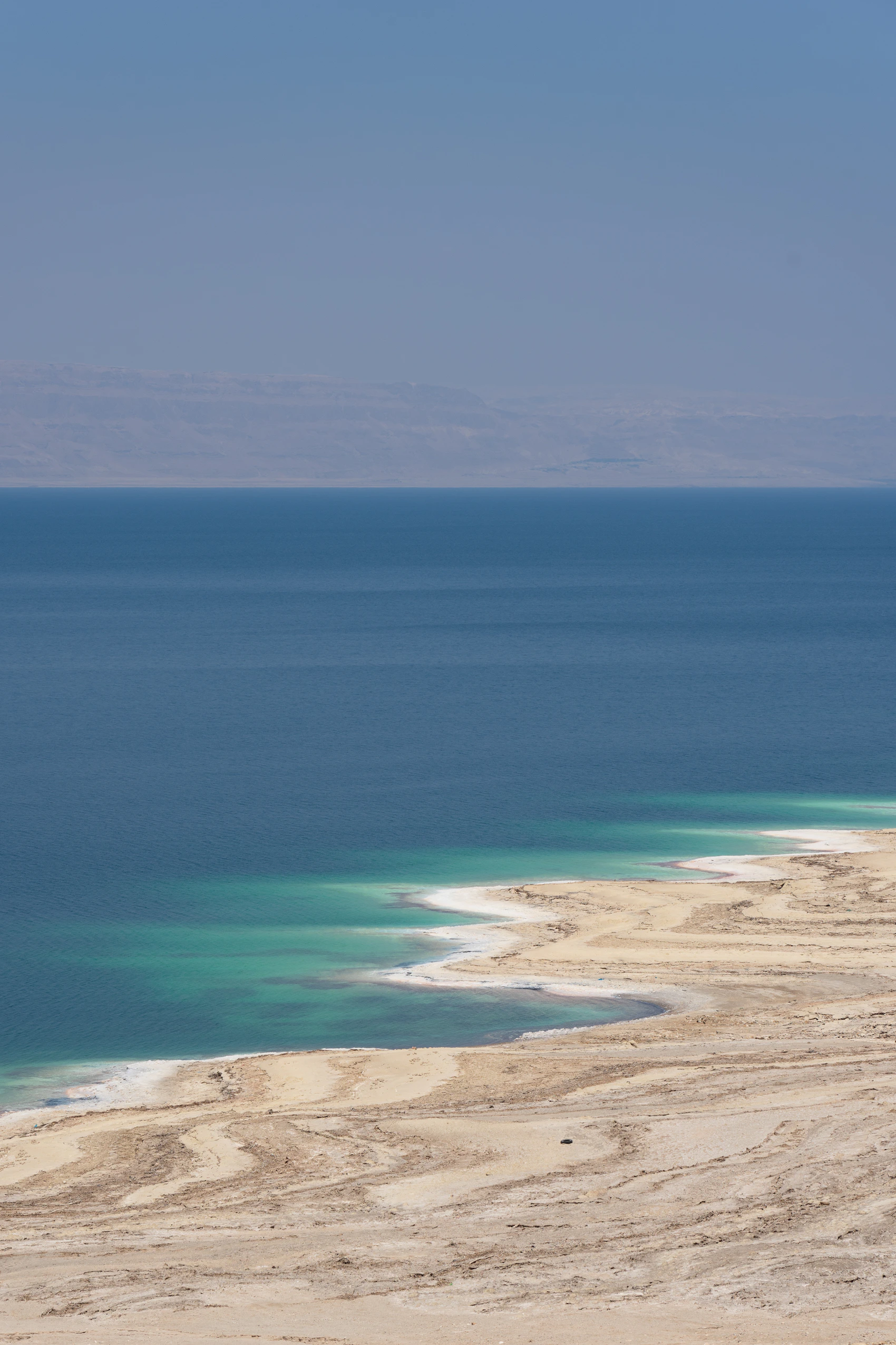 The deep blue water and pale mineral shoreline of the Dead Sea in Jordan