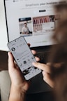 A person holding a cell phone in front of a laptop