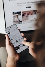 A person holding a cell phone in front of a laptop
