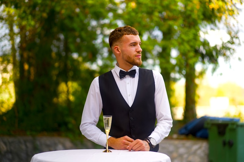 A man in a tuxedo standing at a table with a glass of wine