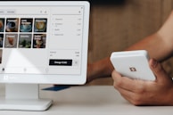 A person holding a cell phone next to a computer monitor