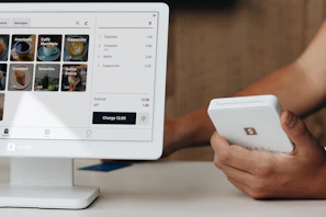 A person holding a cell phone next to a computer monitor