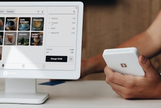 A person holding a cell phone next to a computer monitor