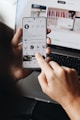 A person holding a cell phone in front of a laptop