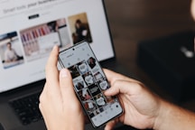 A person holding a cell phone in front of a laptop