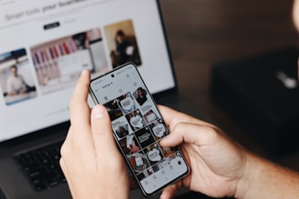 A person holding a cell phone in front of a laptop