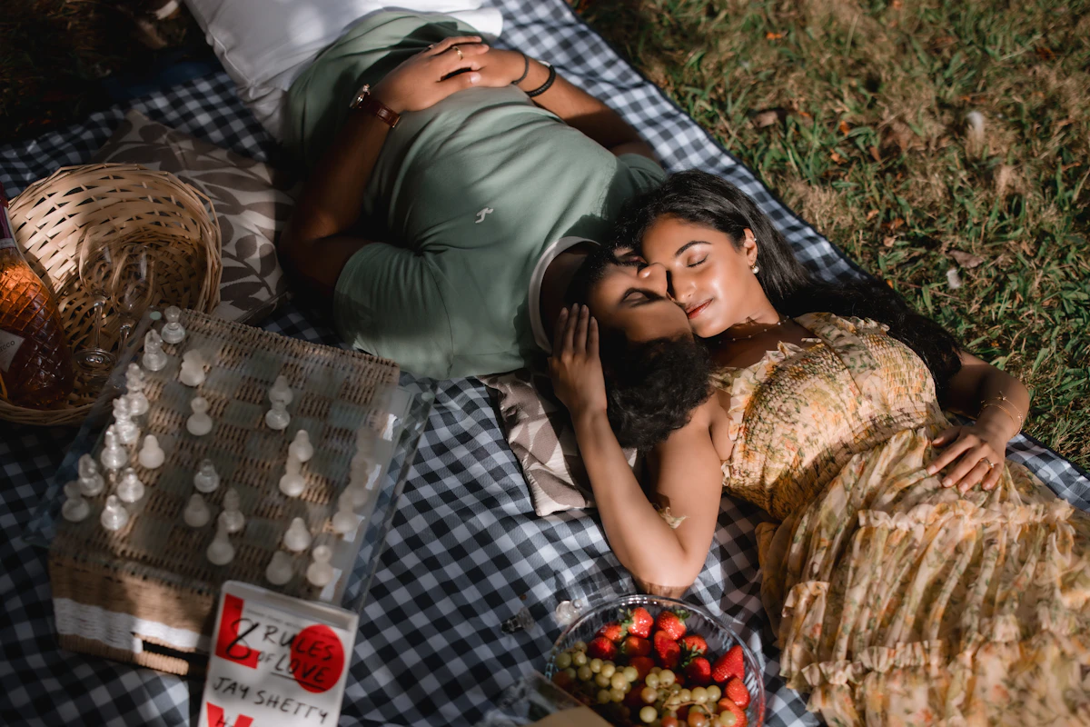 Couple relaxing together on a checkered picnic blanket in a park with fruit and a chess set