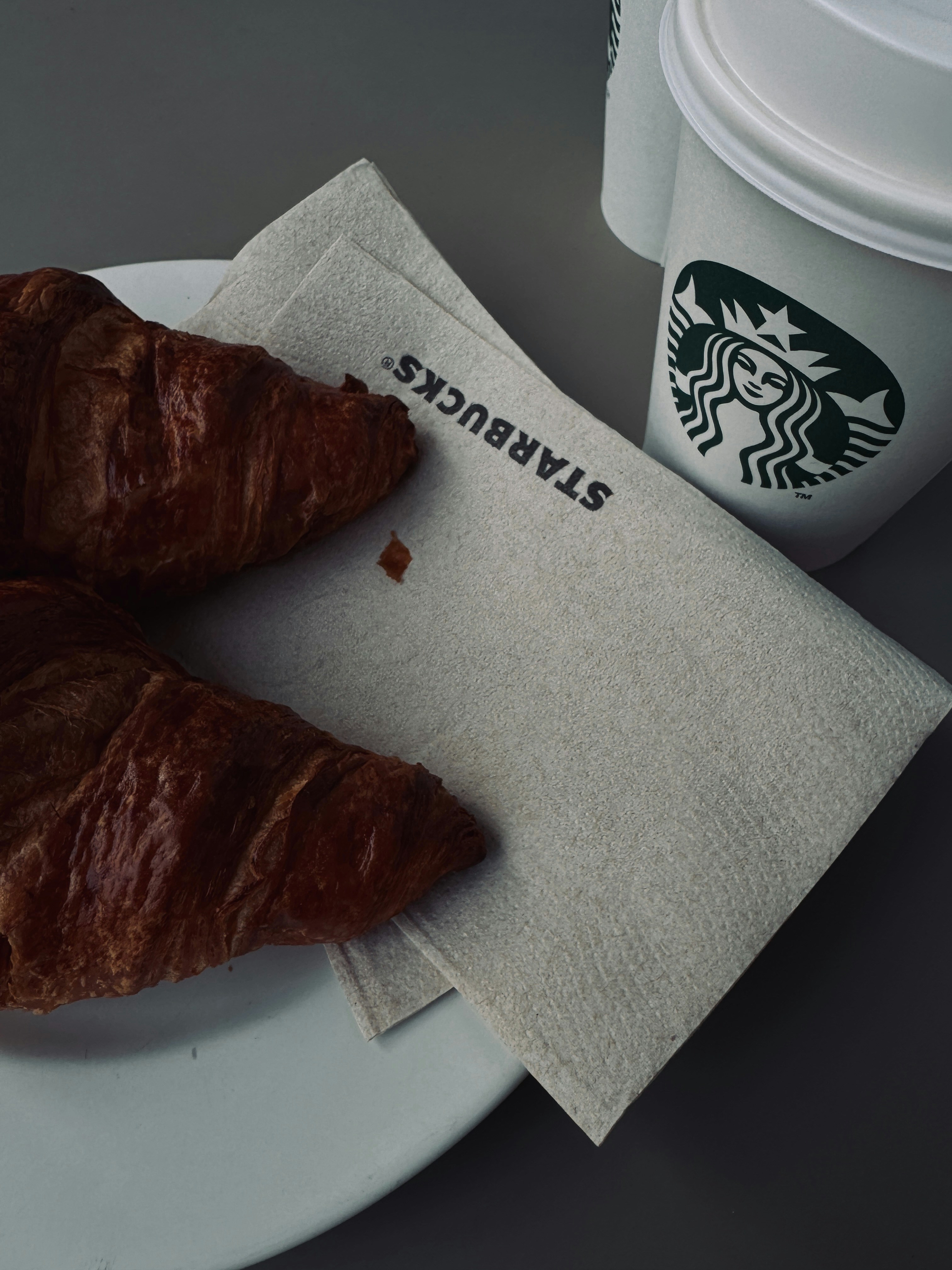 Two croissants on a plate next to a starbucks cup