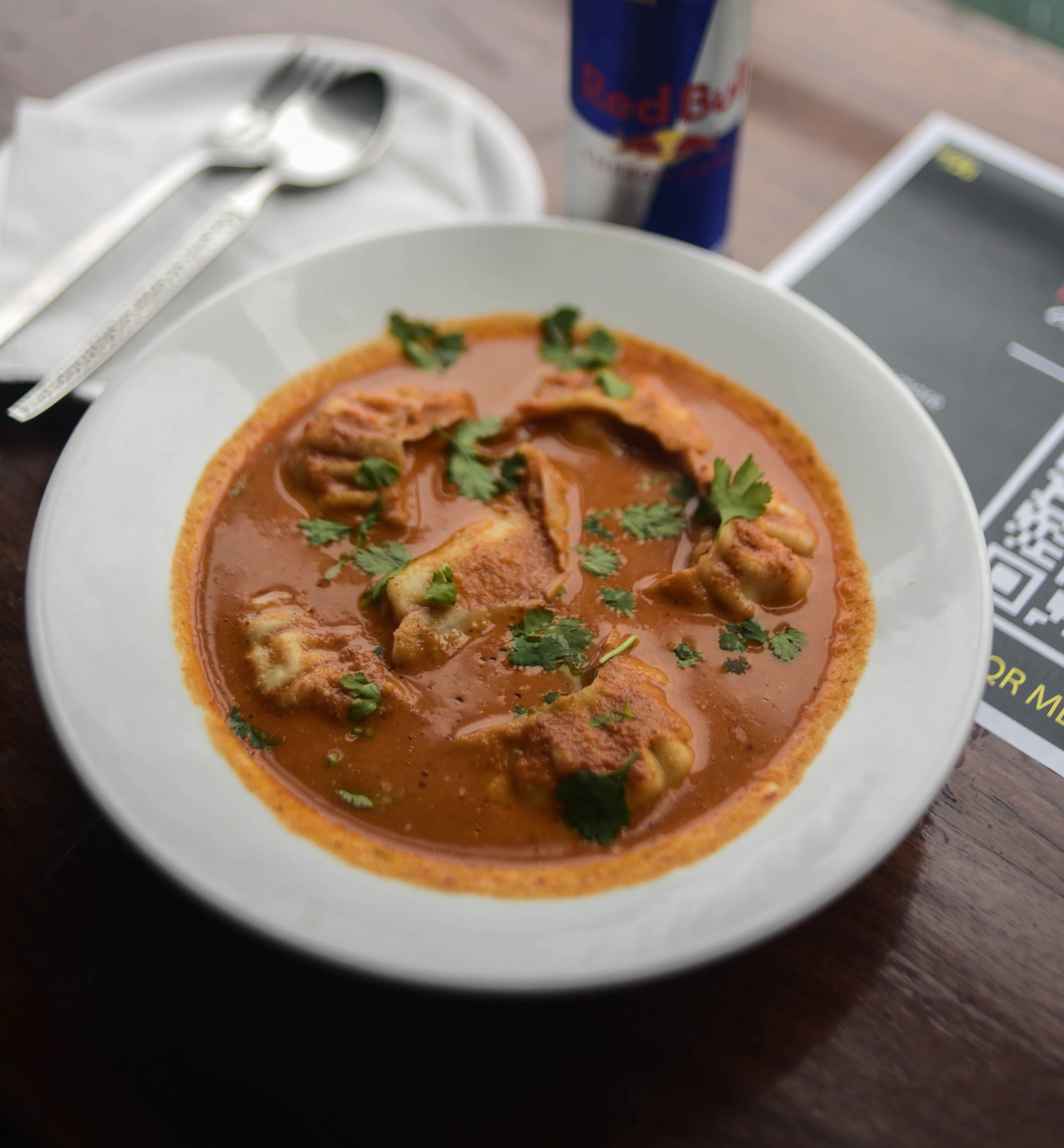 Momo dumplings in a bowl of orange-brown tomato and sesame jhol, scattered with cilantro