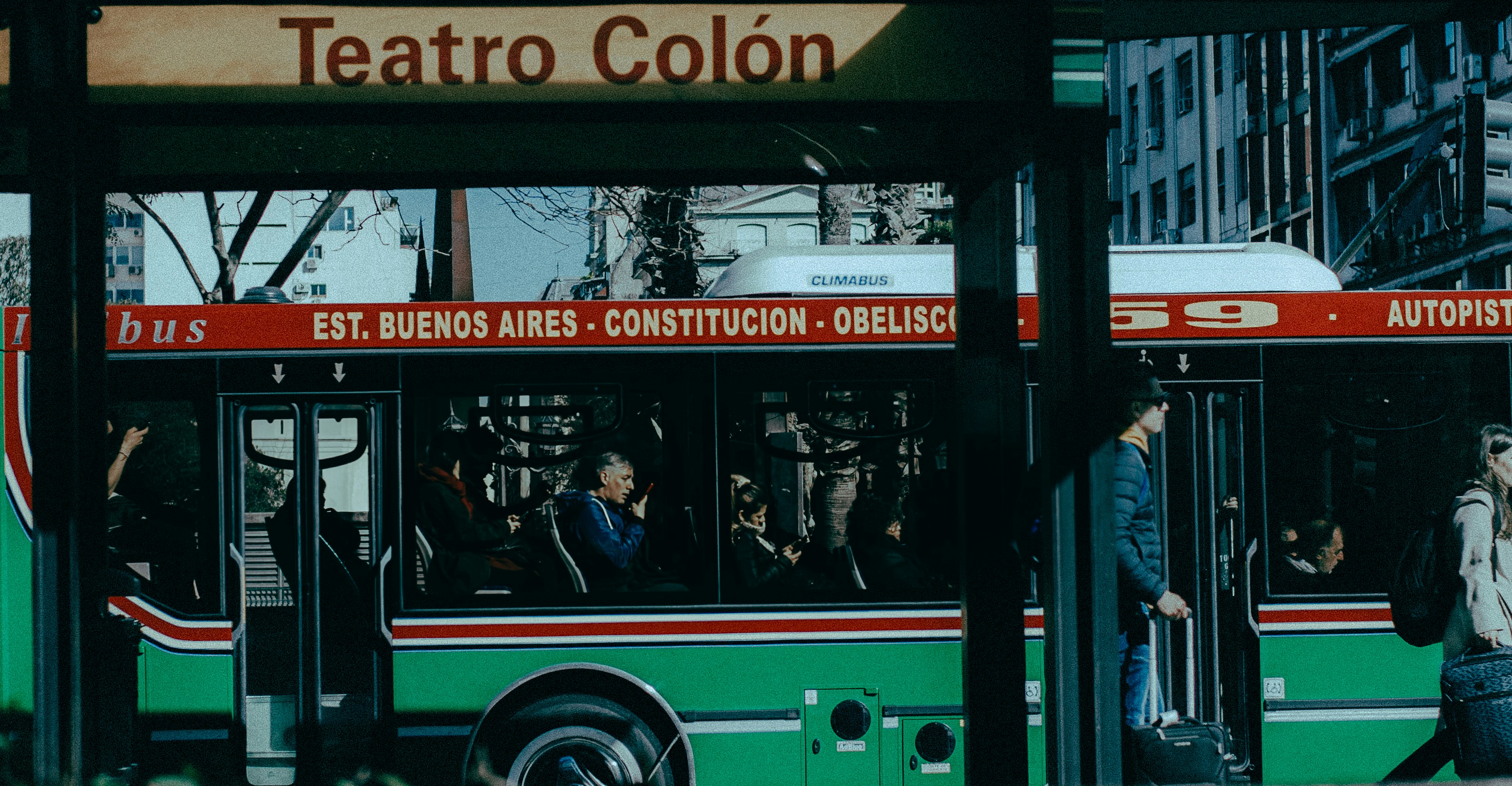 A green and red bus driving down a street next to tall buildings