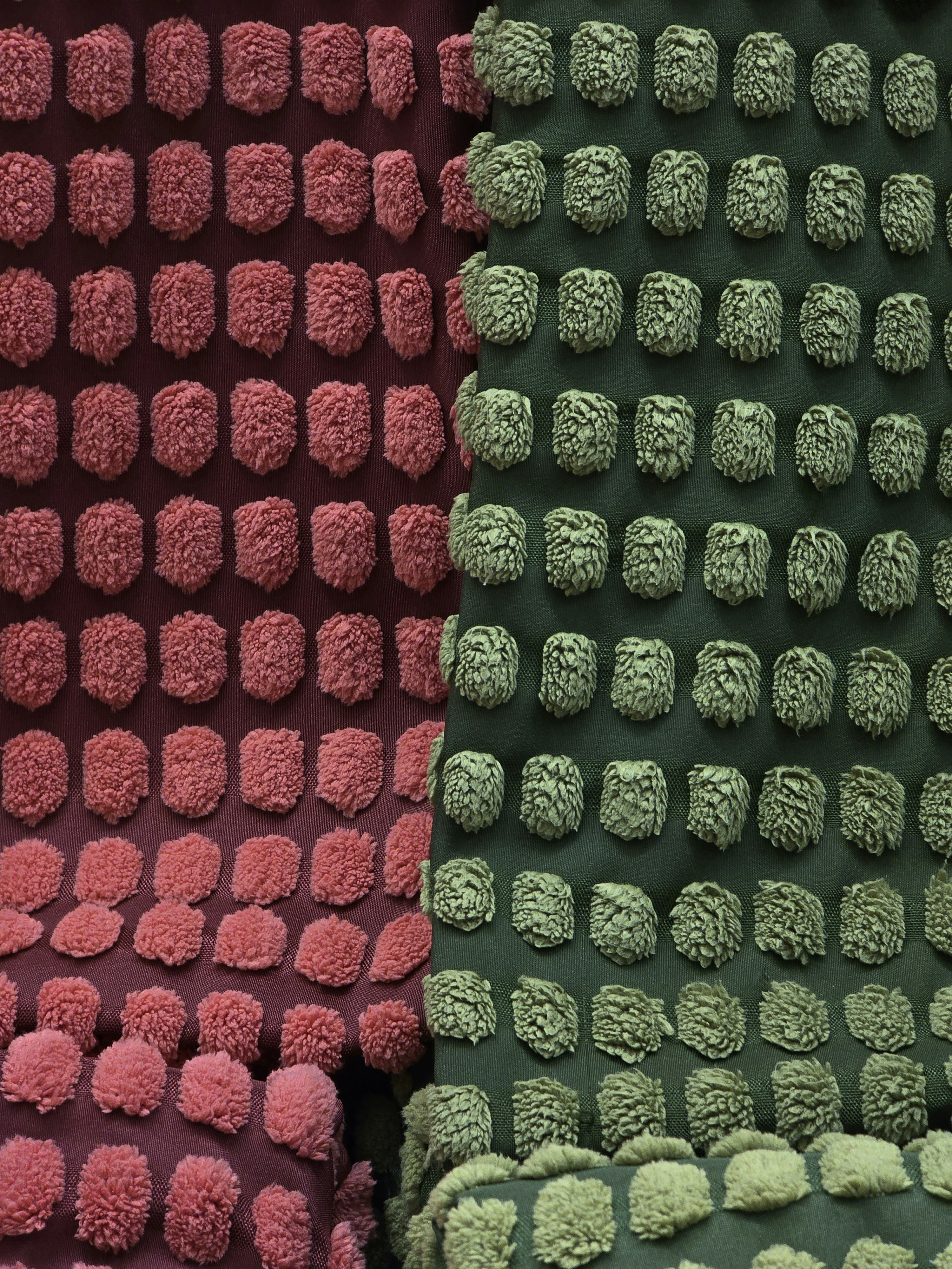 This image showcases two textured fabrics side by side, like a playful meeting of colorful dots. On the left, the maroon base is covered in cheerful pink puffs, while the green fabric on the right sports soft green ones, as if they’re having a quiet conversation in shades of nature and sunset. The raised, fluffy circles almost invite you to reach out and touch them, adding a whimsical, tactile feel to the whole scene. It’s like a cozy duel of colors and textures, with each side showing off its own unique charm.
