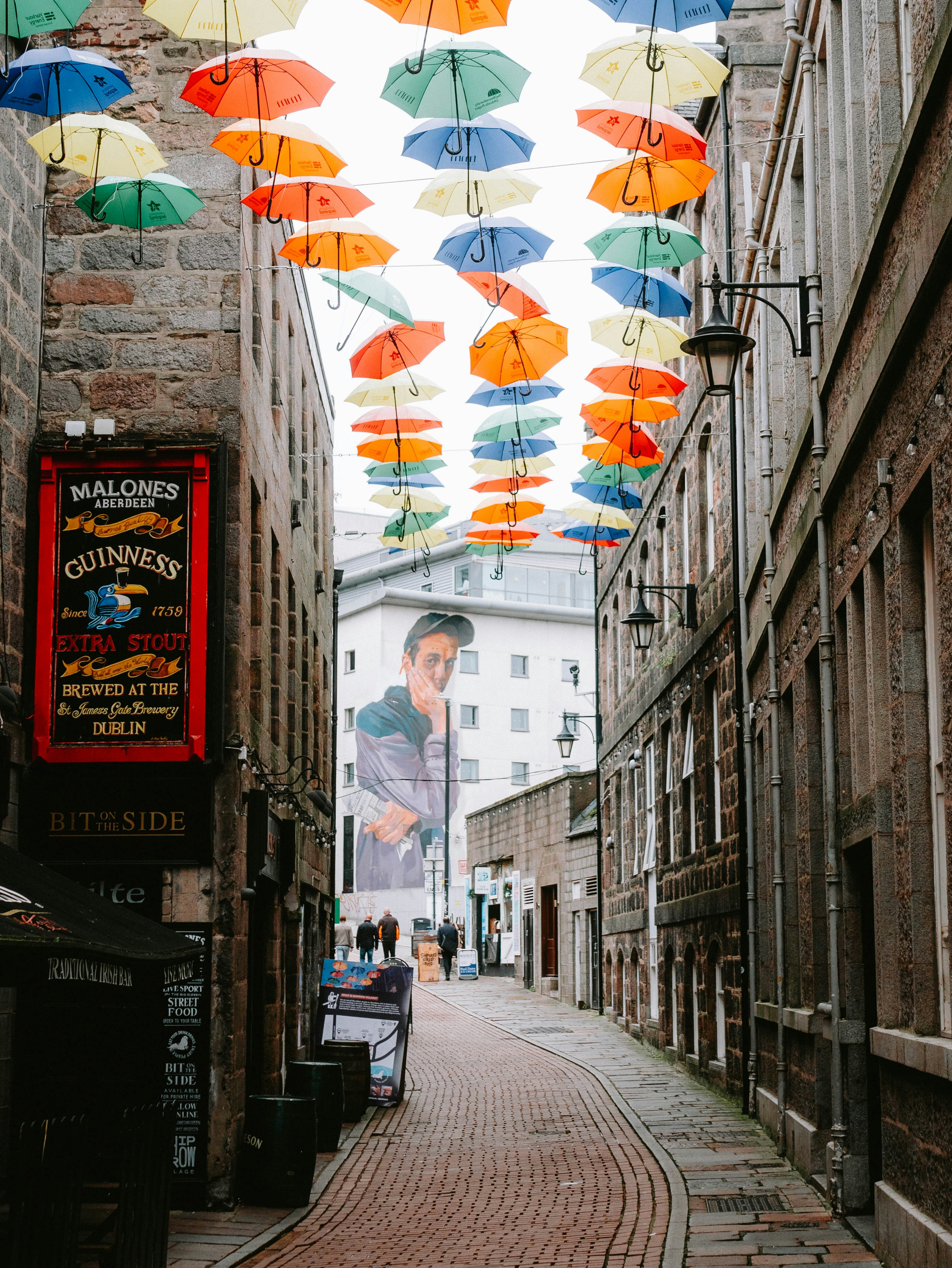A narrow alleyway with many colorful umbrellas hanging from the ceiling