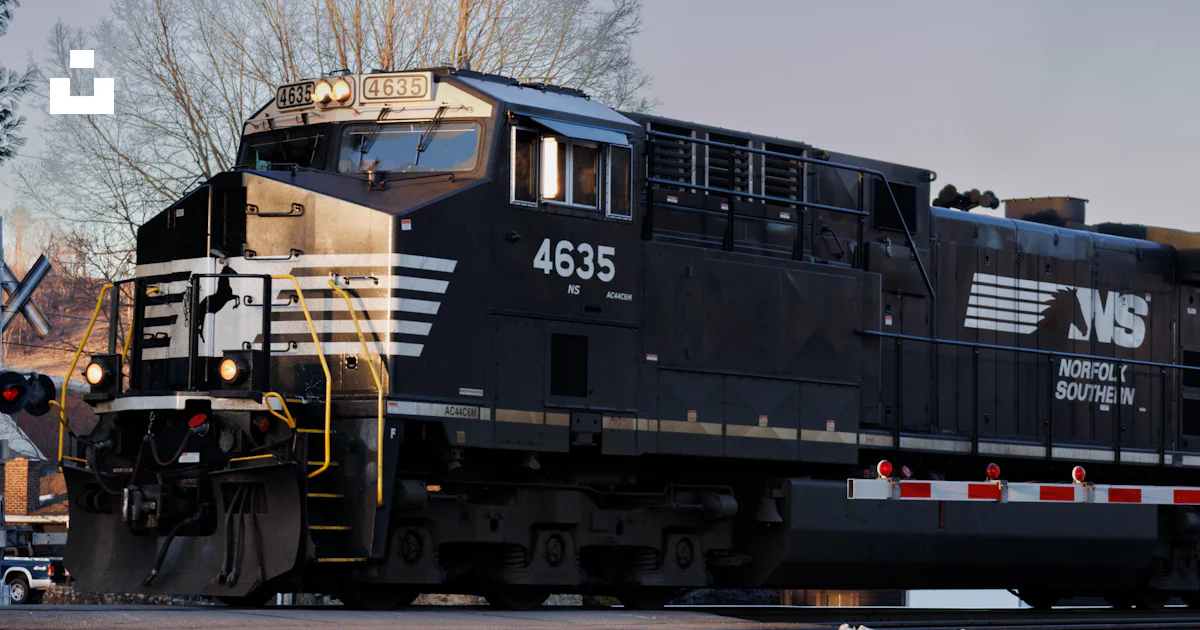 A black train traveling down train tracks next to a forest photo – Free ...