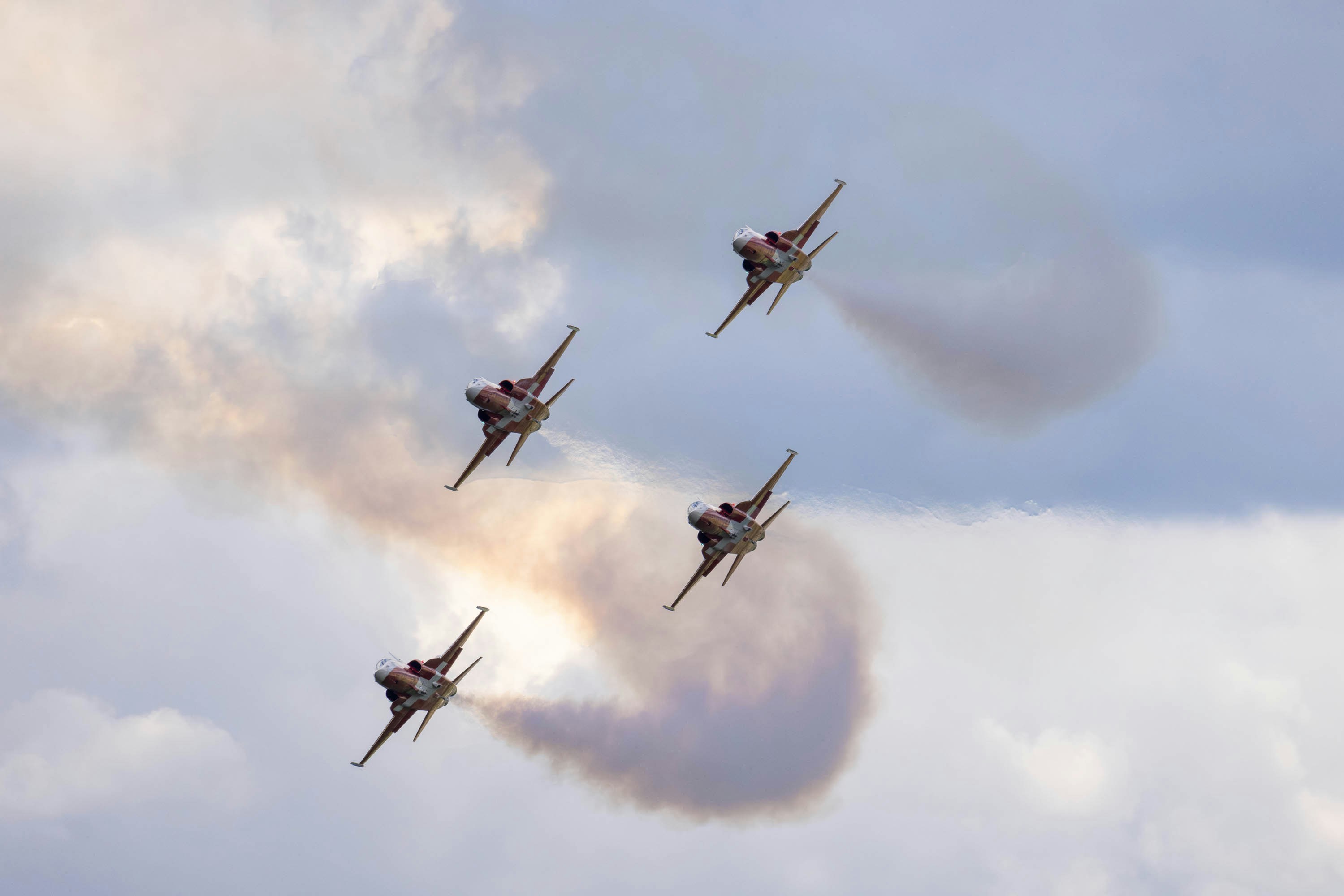 A group of jets flying through a cloudy sky, Swiss acrobatic patrol in formation with four F5 in turn and climb.
