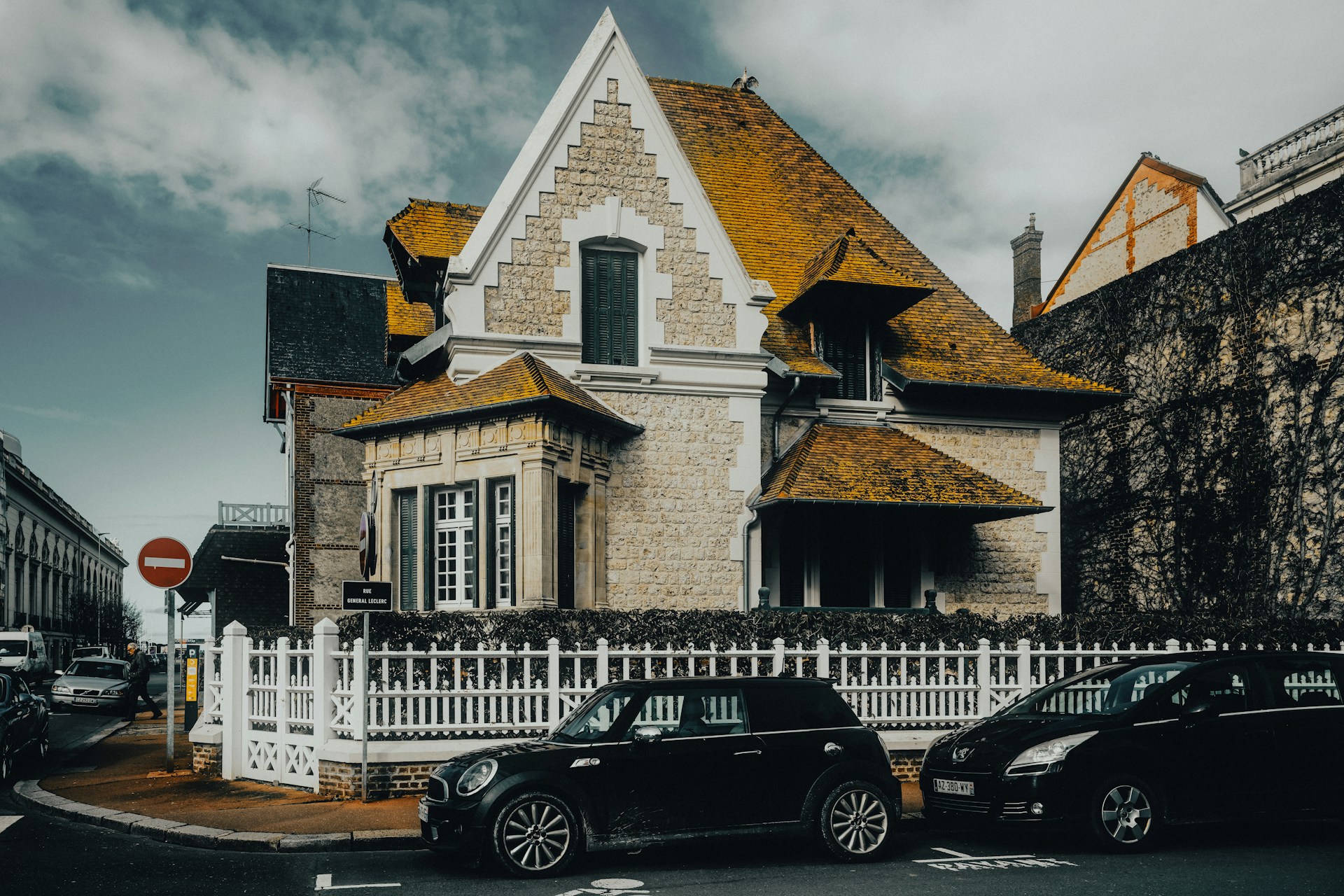 A house with a white picket fence and cars parked in front of it