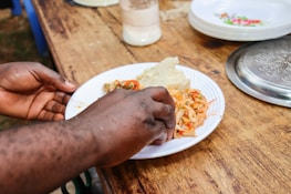 A person holding a plate of food on a table