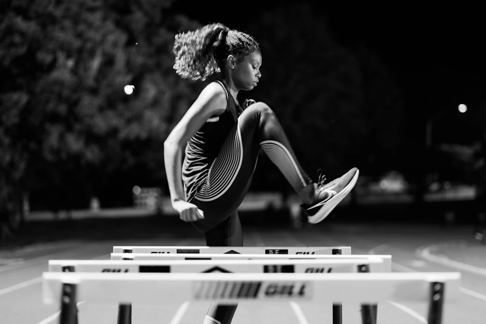 A Black woman clearing a hurdle on an athletics track