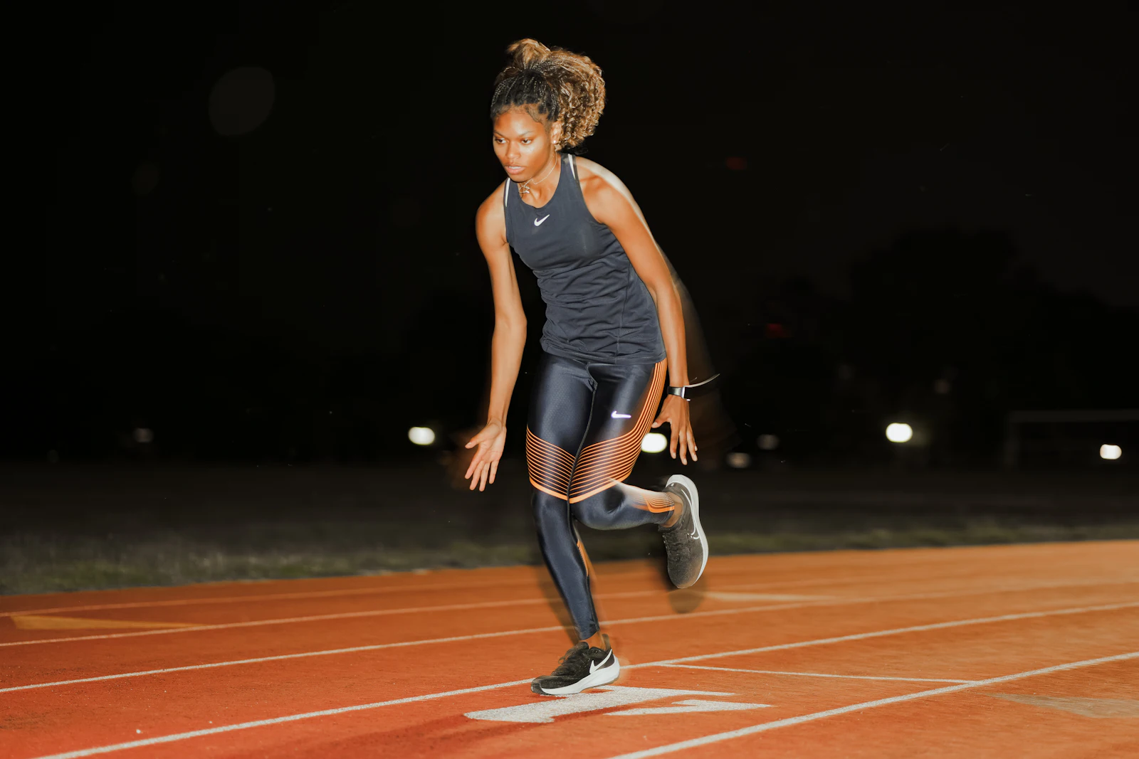 Atleta em arrancada explosiva na pista à noite, luz dramática