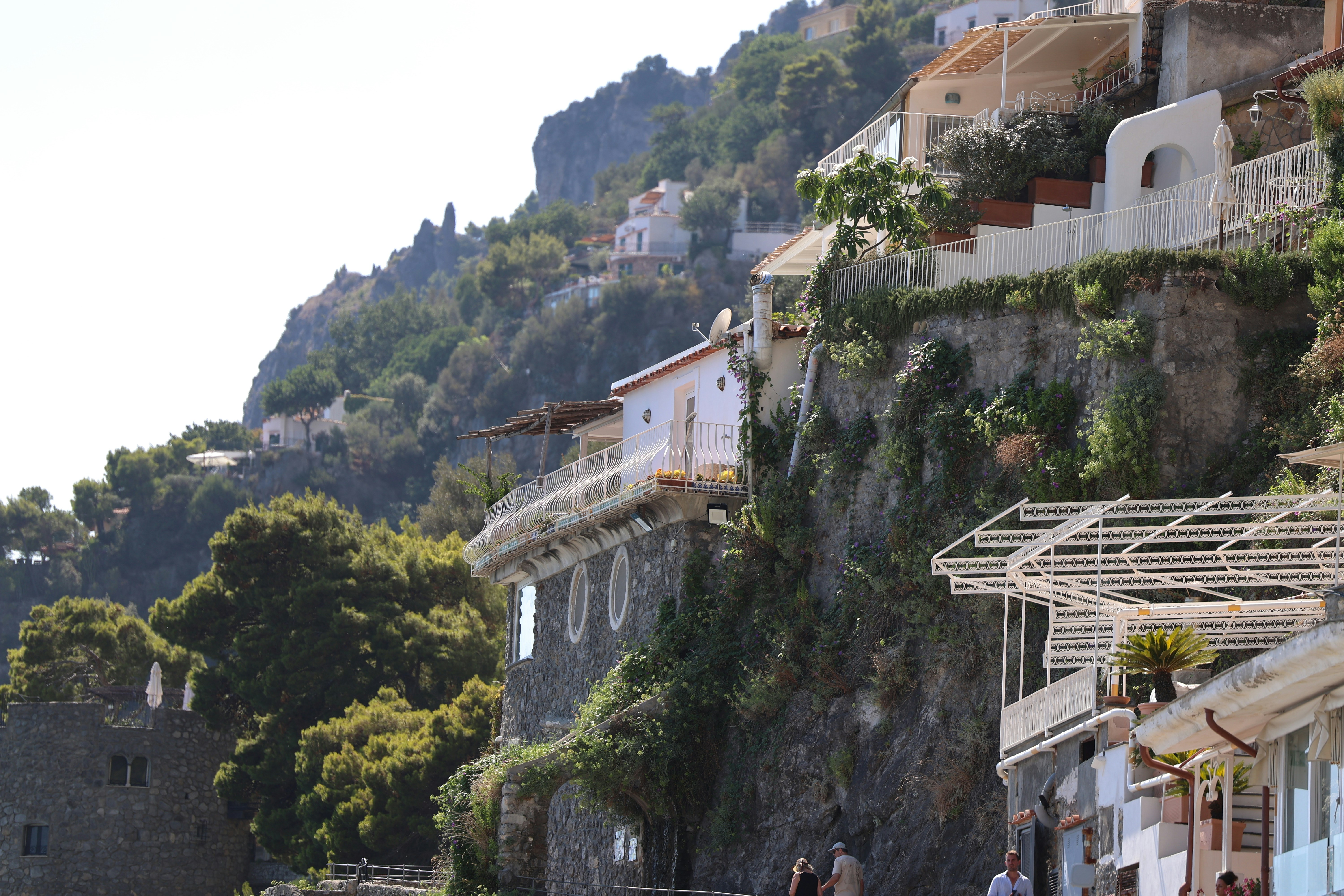 A group of people walking down a street next to a hillside