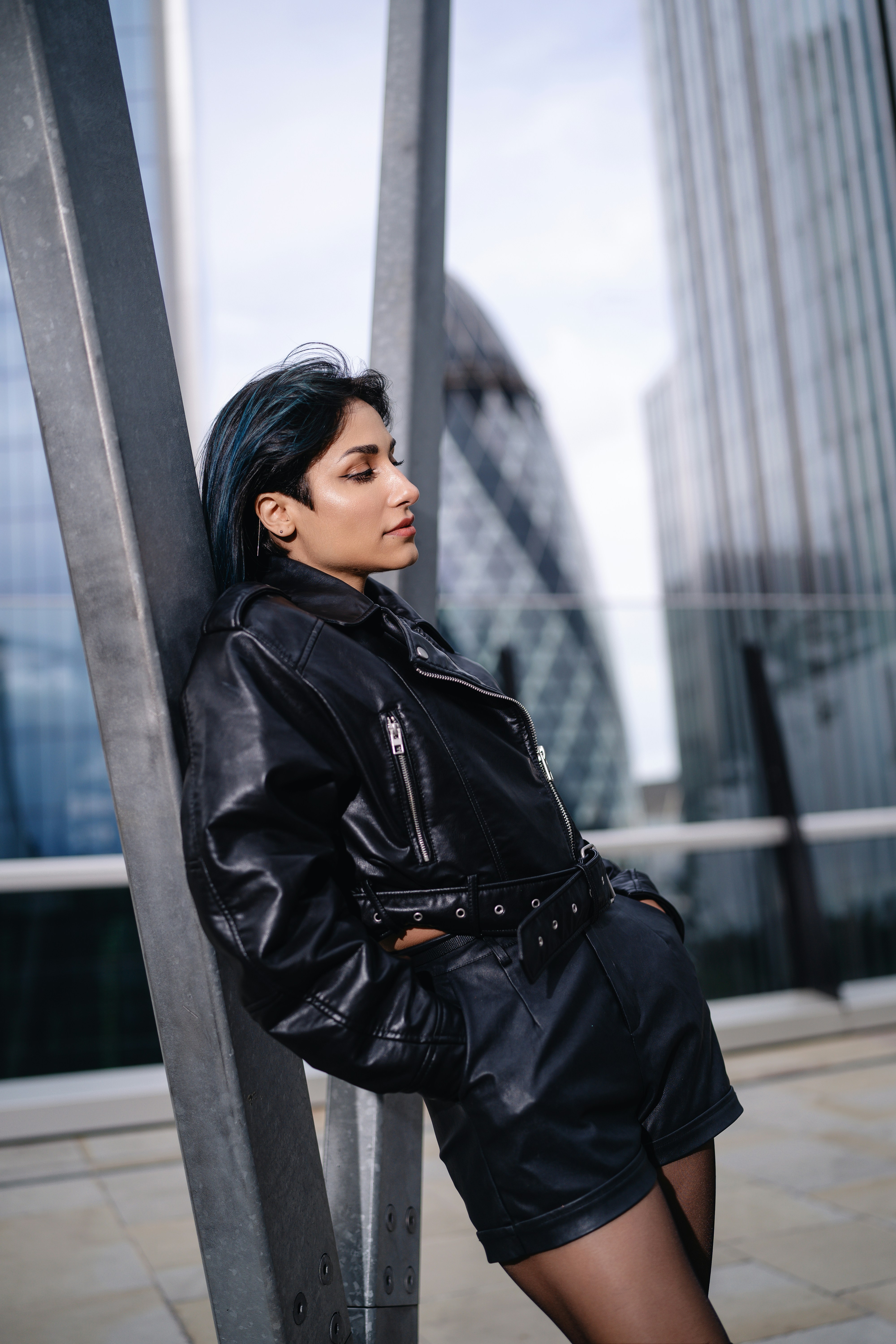 A woman in a black leather jacket leaning against a pole
