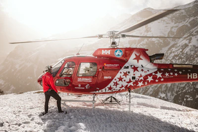 A man standing next to a red helicopter on top of a snow covered mountain