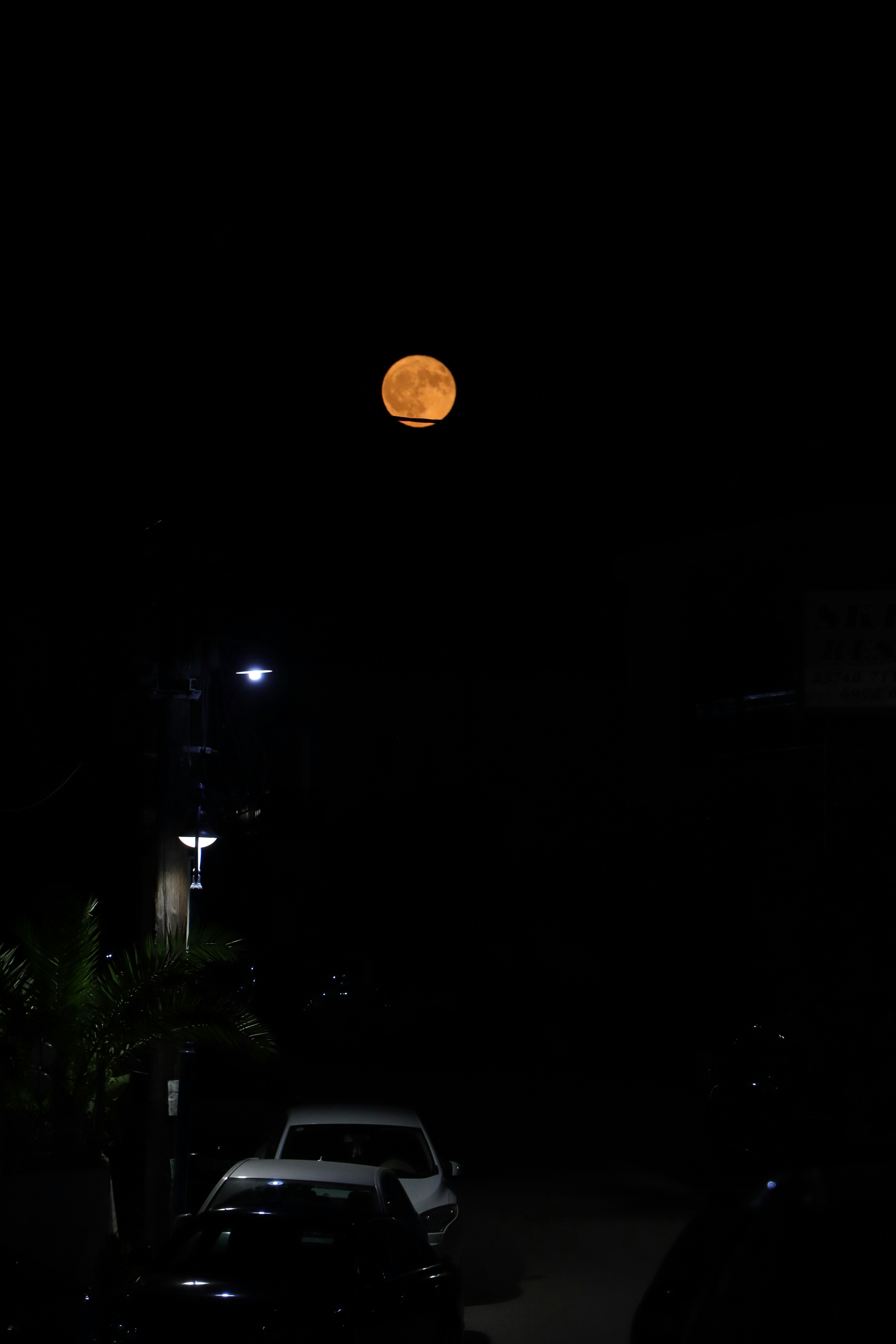 A car parked on a street at night with a full moon in the background