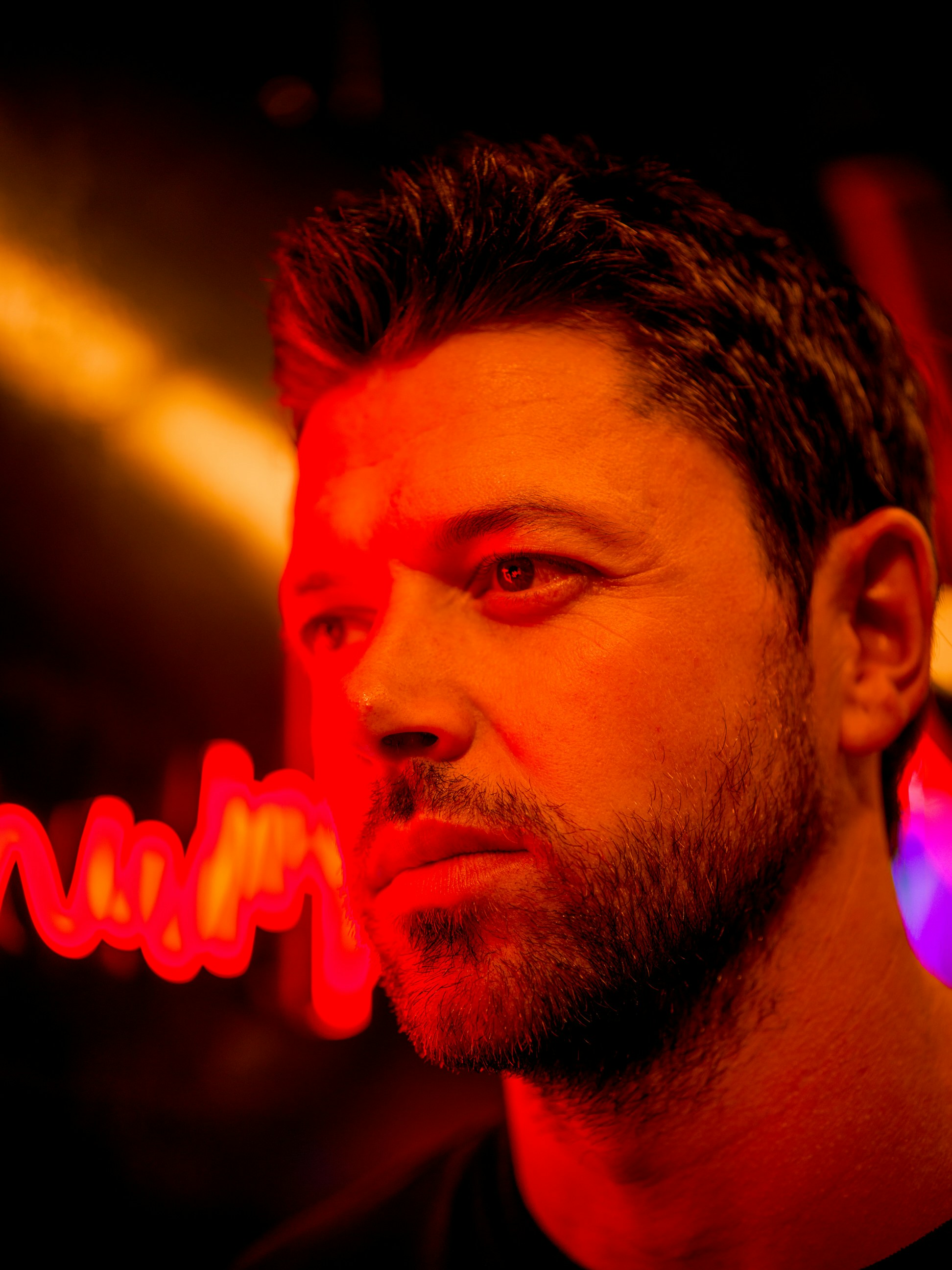 A man in a dark room with a neon sign in the background