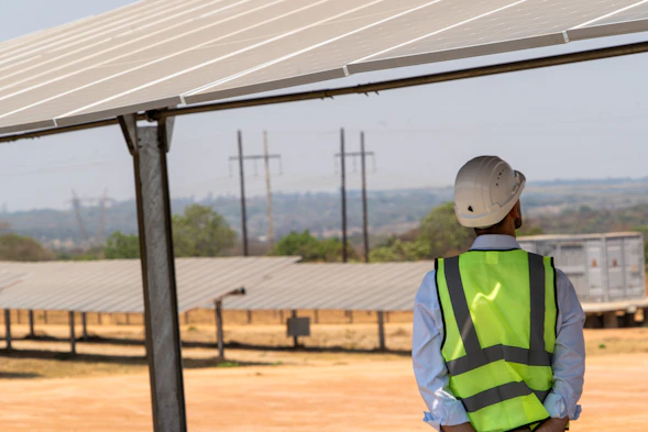 A man in a safety vest standing under a solar panel