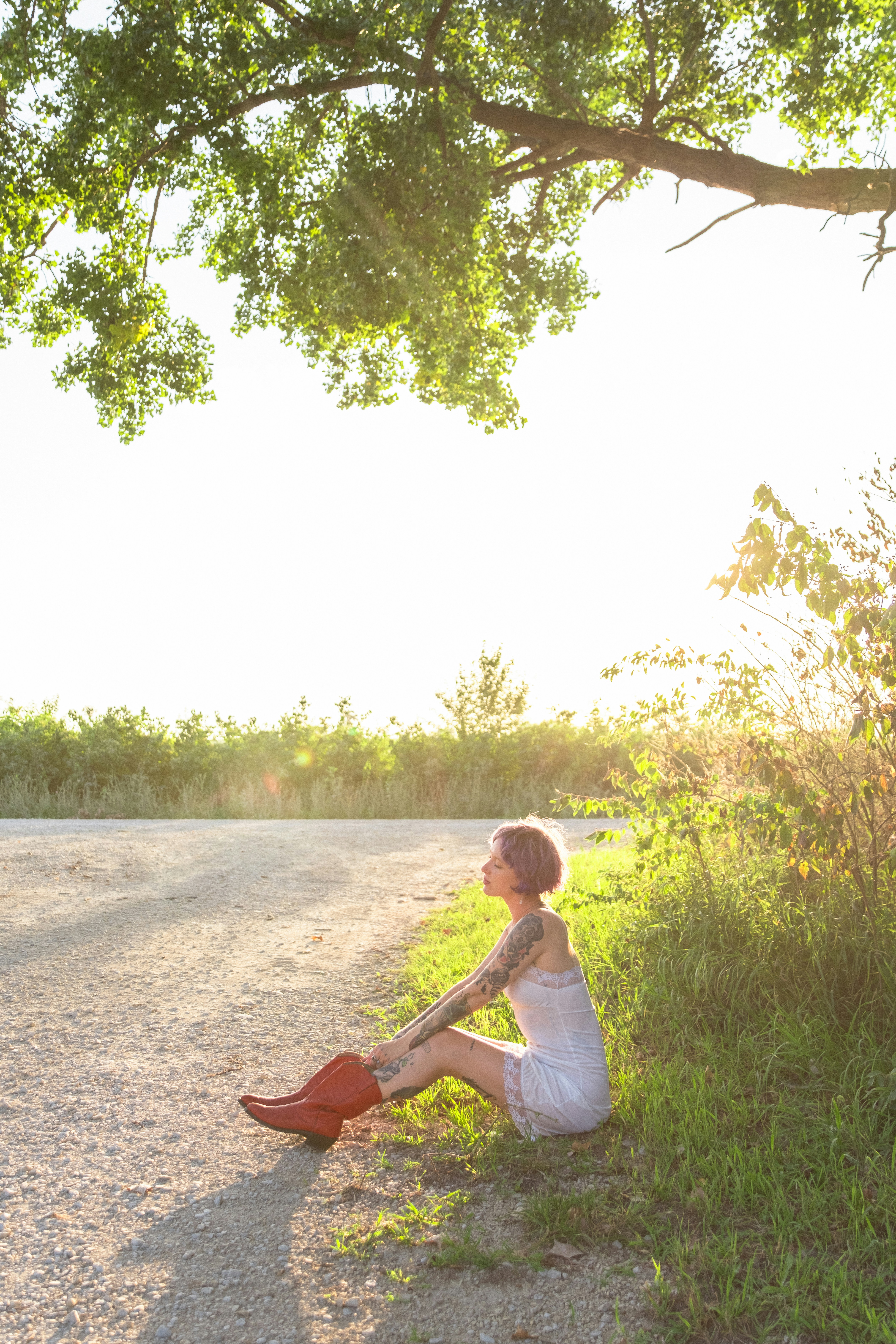 A woman sitting on the side of a road next to a tree