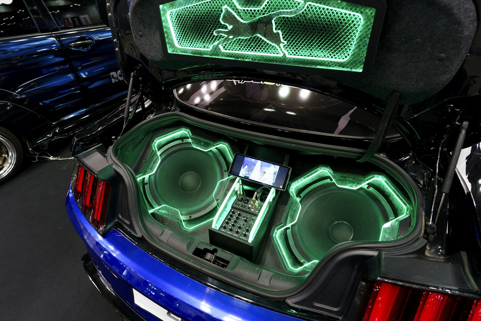 Custom car trunk build featuring two large subwoofers with green LED lighting showing a professional car audio installation