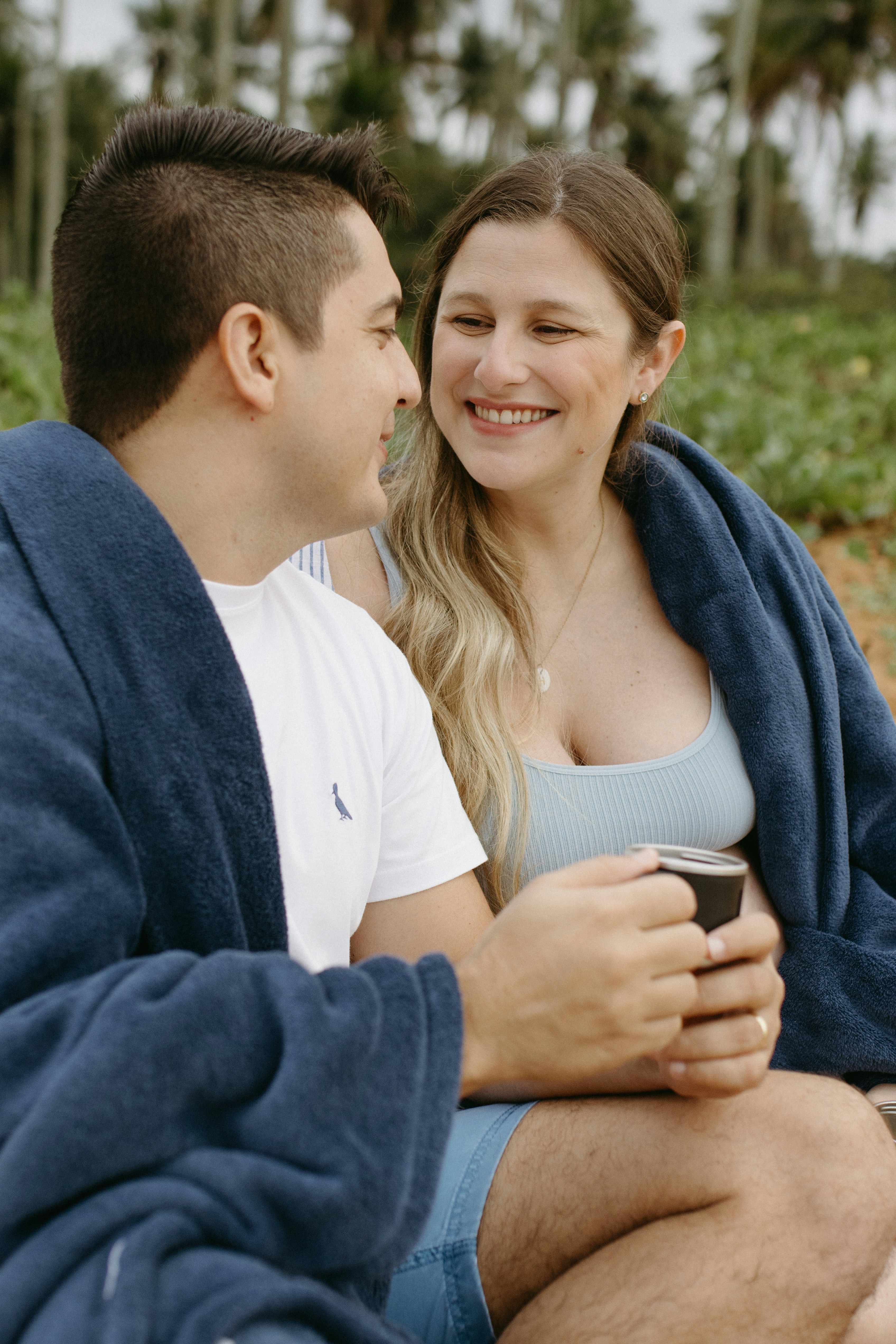 A man and a woman sitting on a beach under a blanket