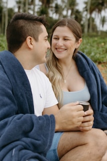 A man and a woman sitting on a beach under a blanket