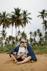 A man and a woman sitting on a beach with palm trees in the background
