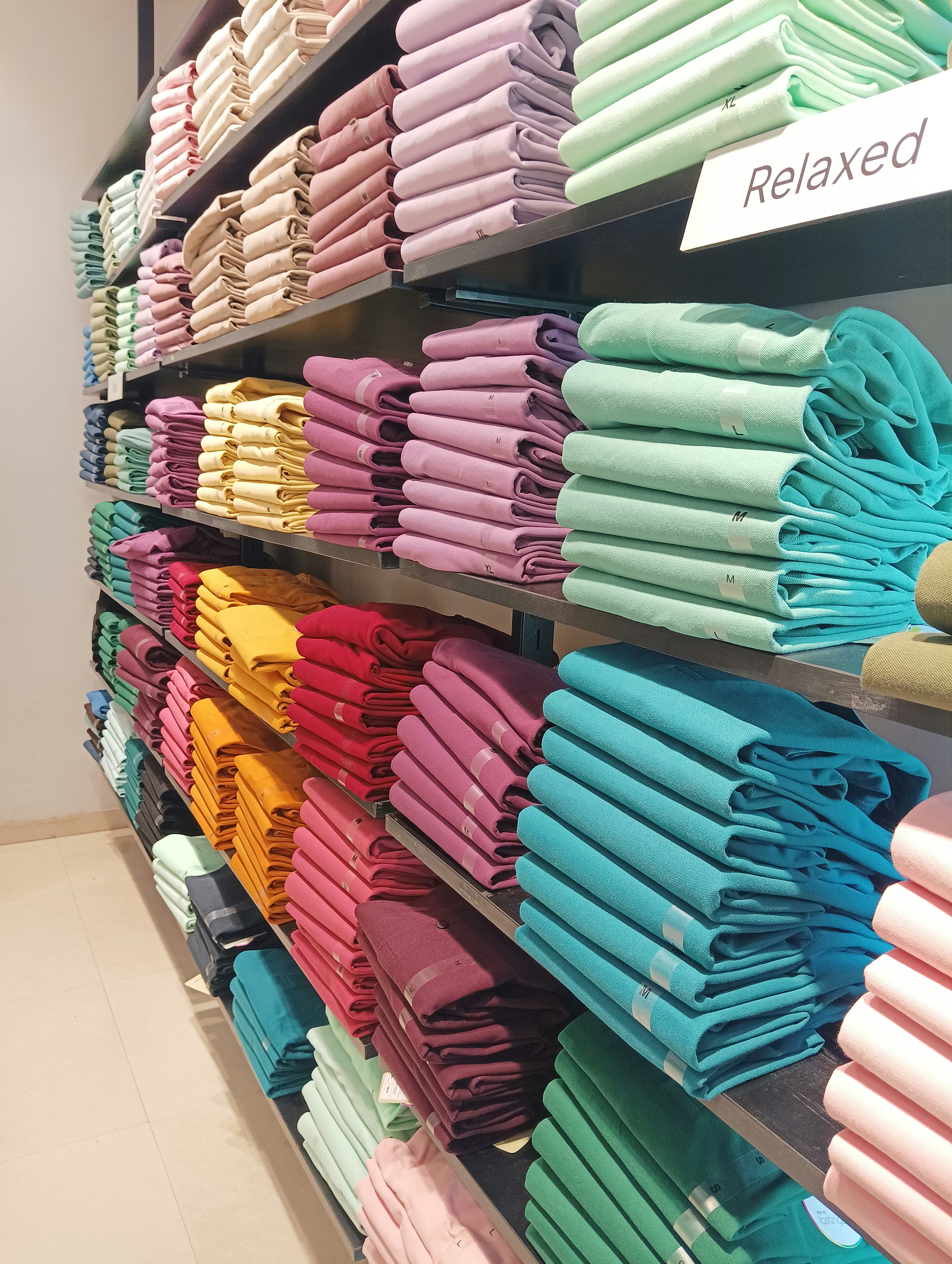 Neatly folded pastel tops on white shelf, bright natural light