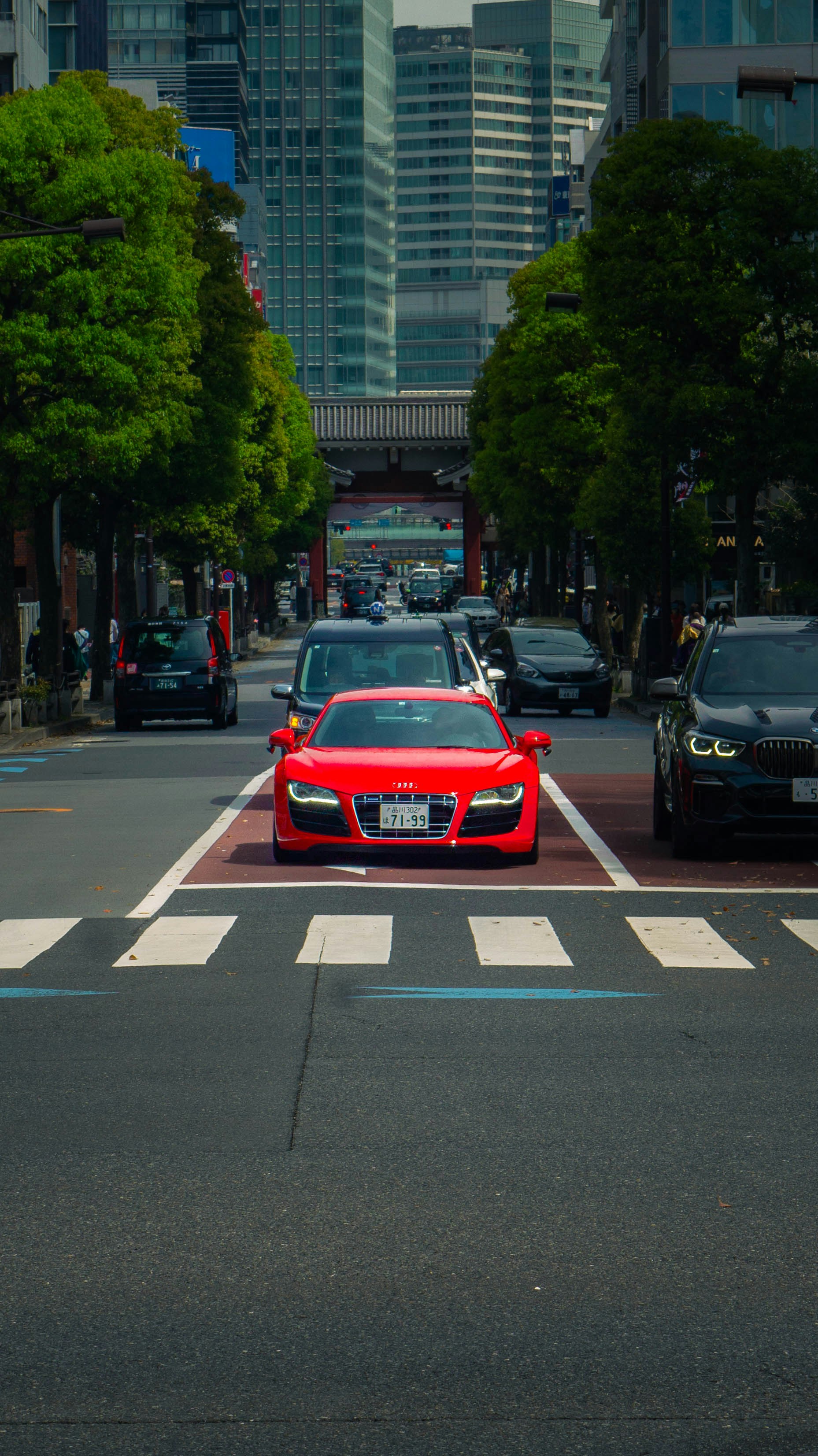 A red car driving down a street next to tall buildings