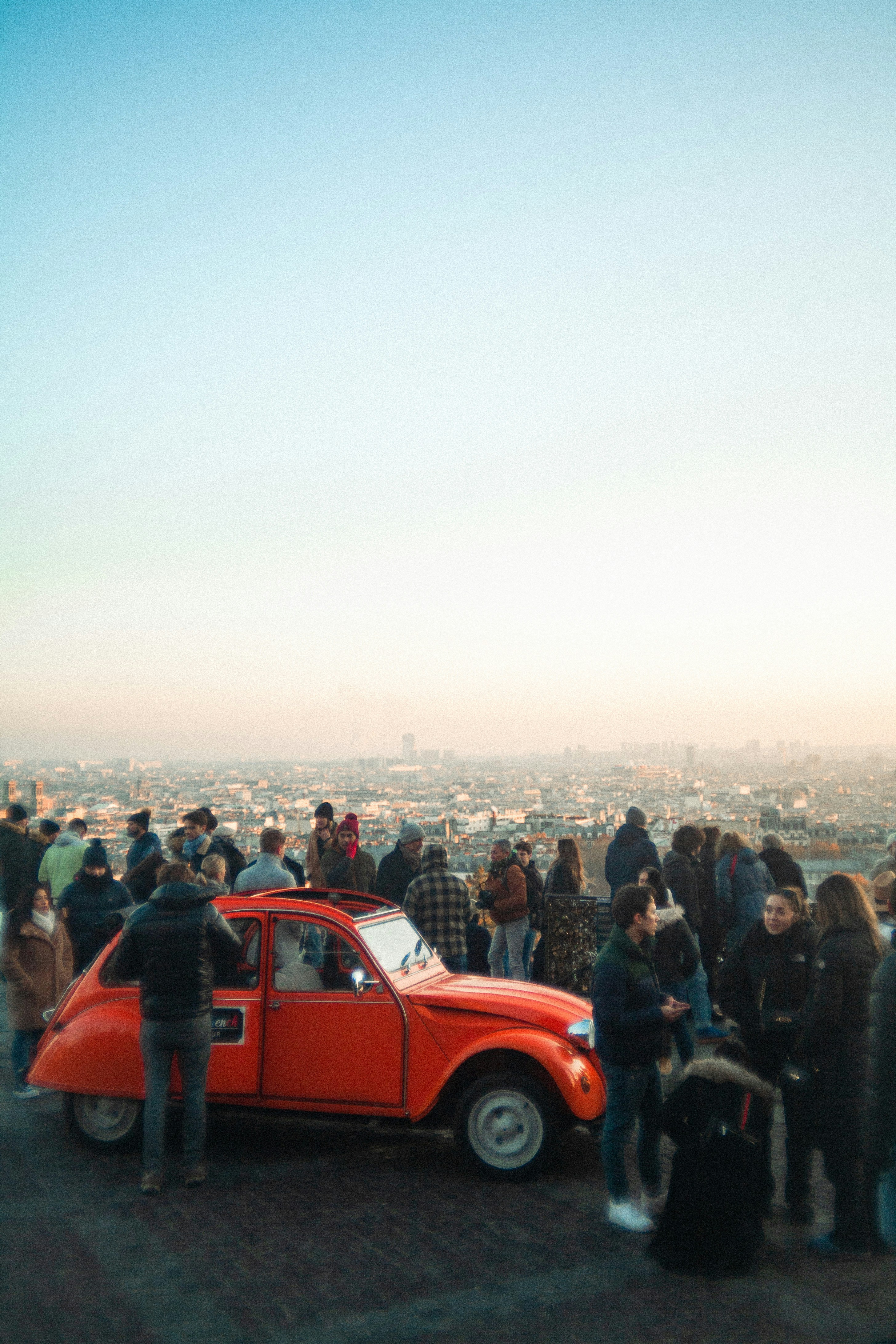 A group of people standing around a red car