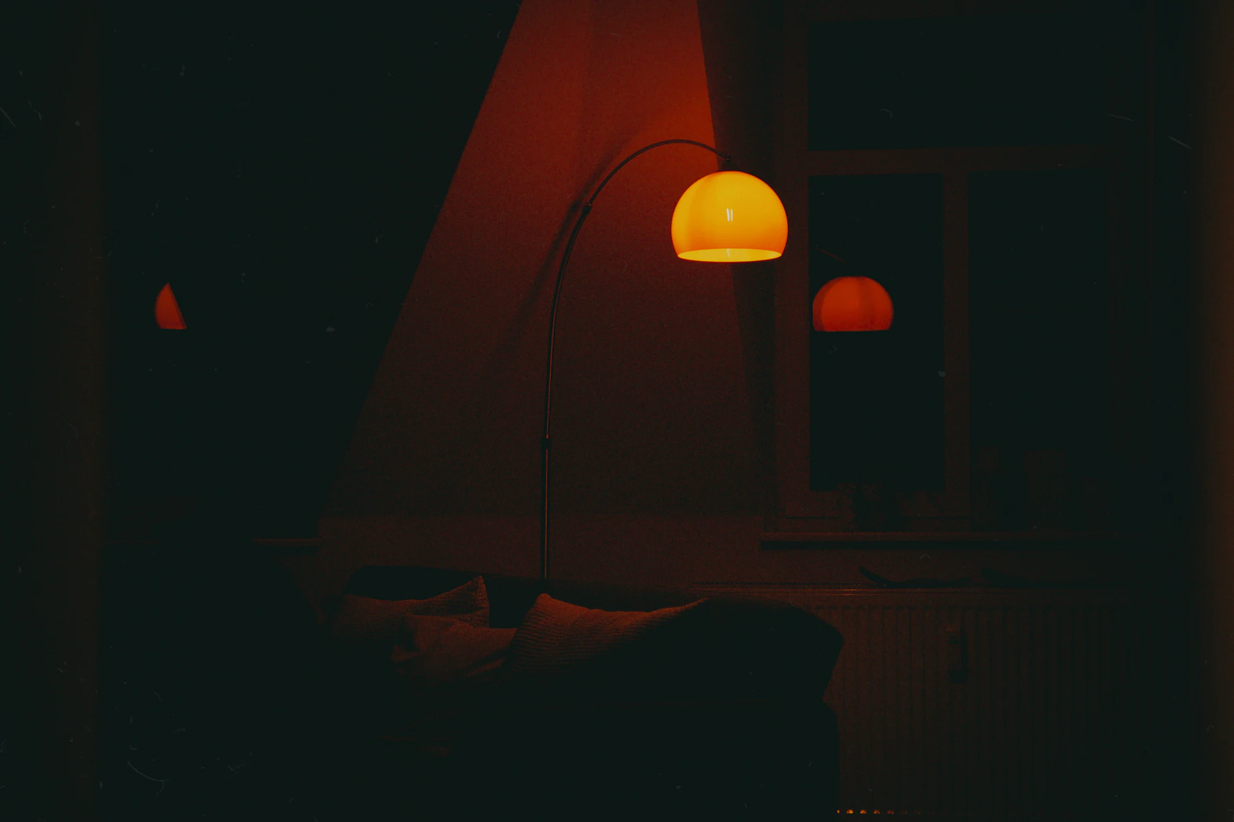 Arc floor lamp glowing amber in a dark living room corner at night