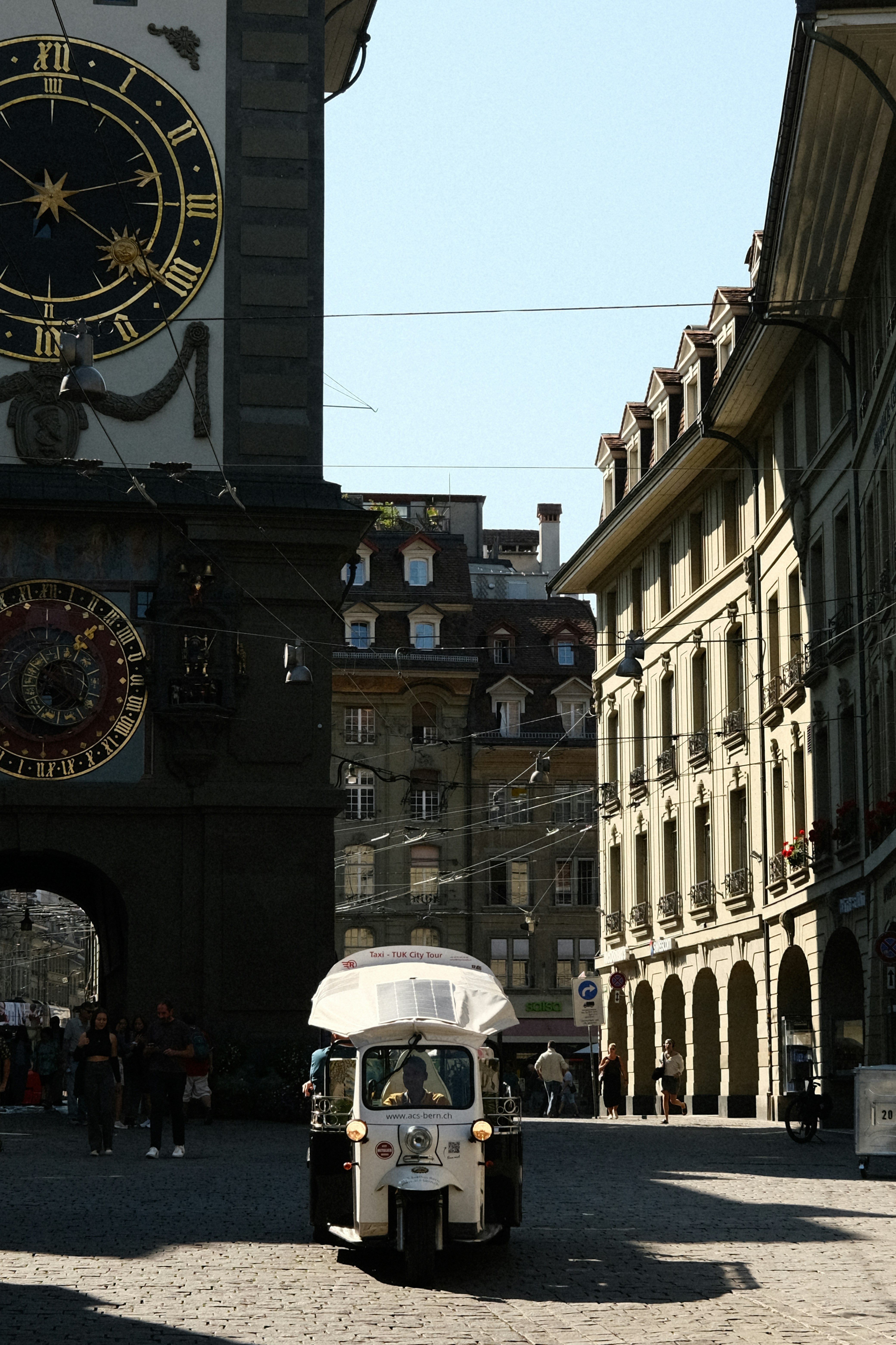 Un pequeño coche circulando por una calle junto a una torre del reloj