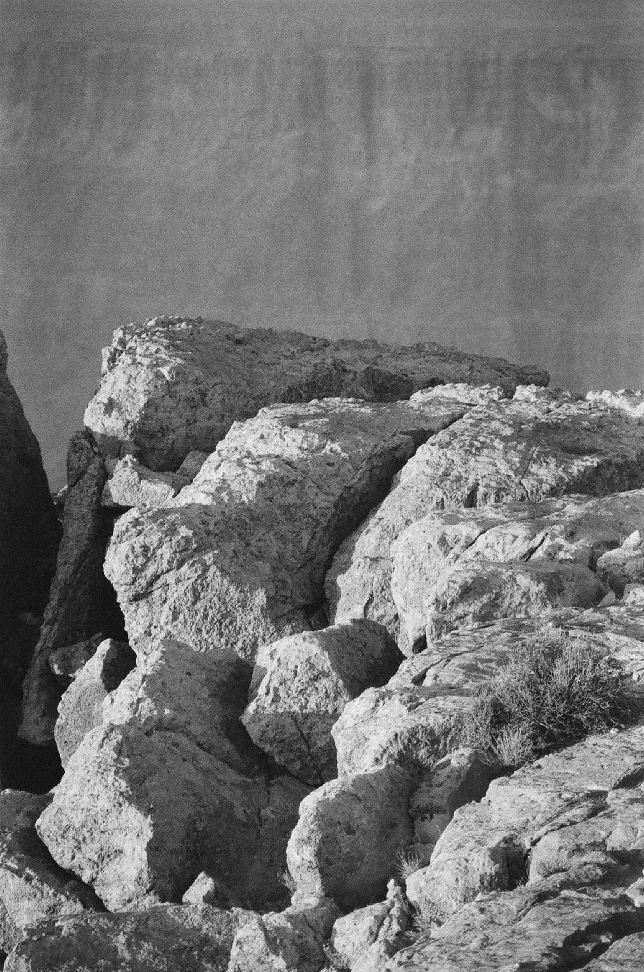 A black and white photo of a man sitting on a rock