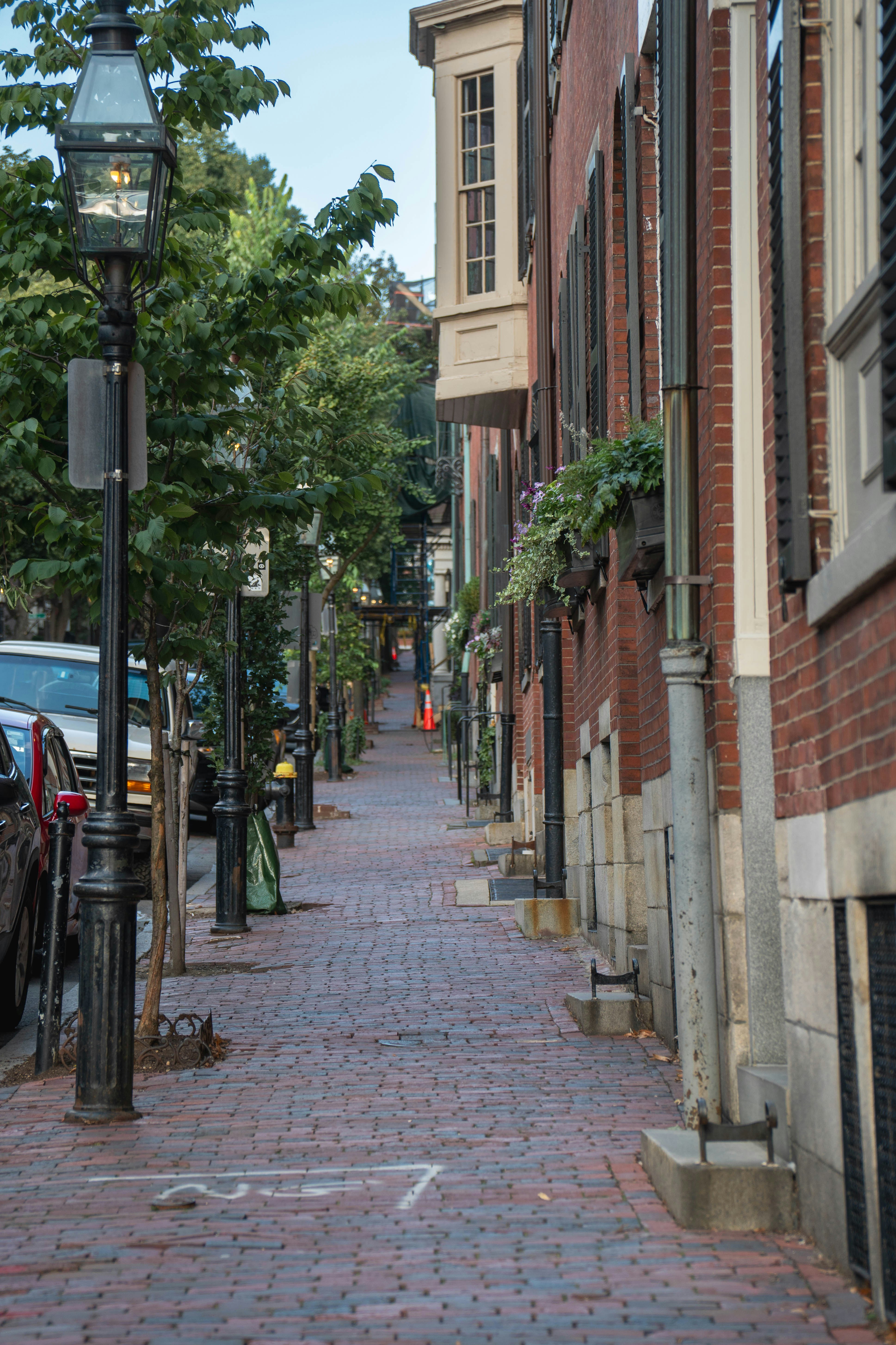 A street light on a brick sidewalk next to parked cars