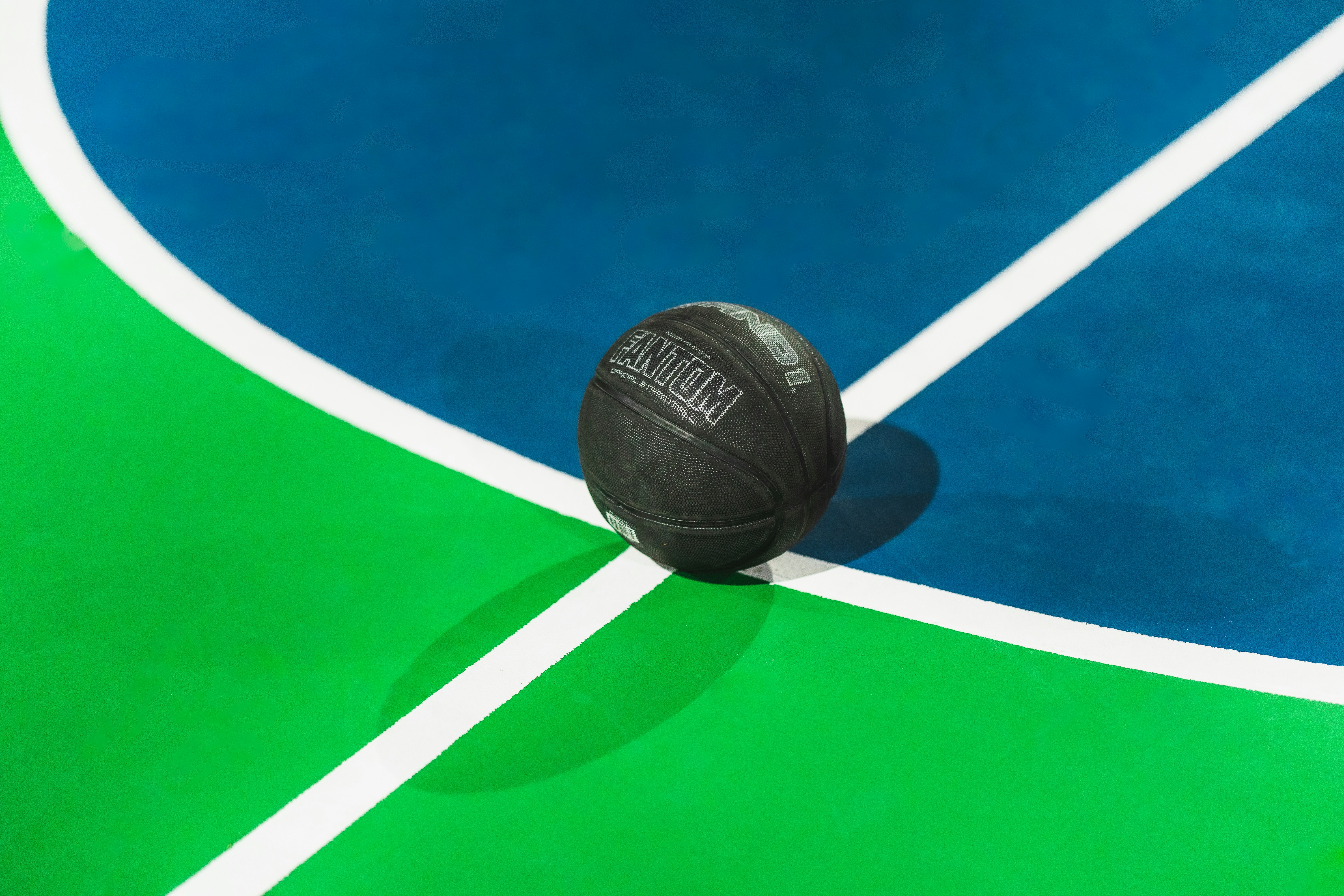A black ball sitting on top of a green and blue basketball court