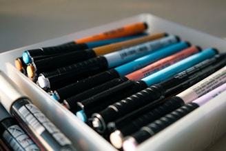 A white container filled with lots of different colored pens