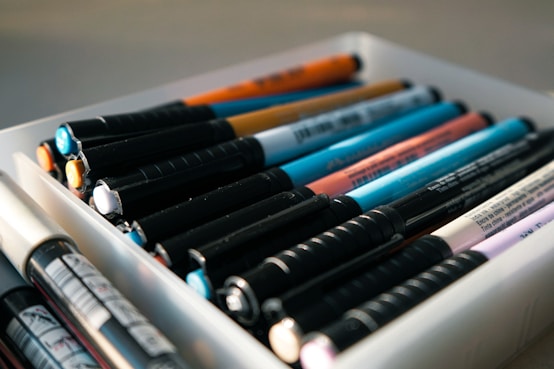 A white container filled with lots of different colored pens