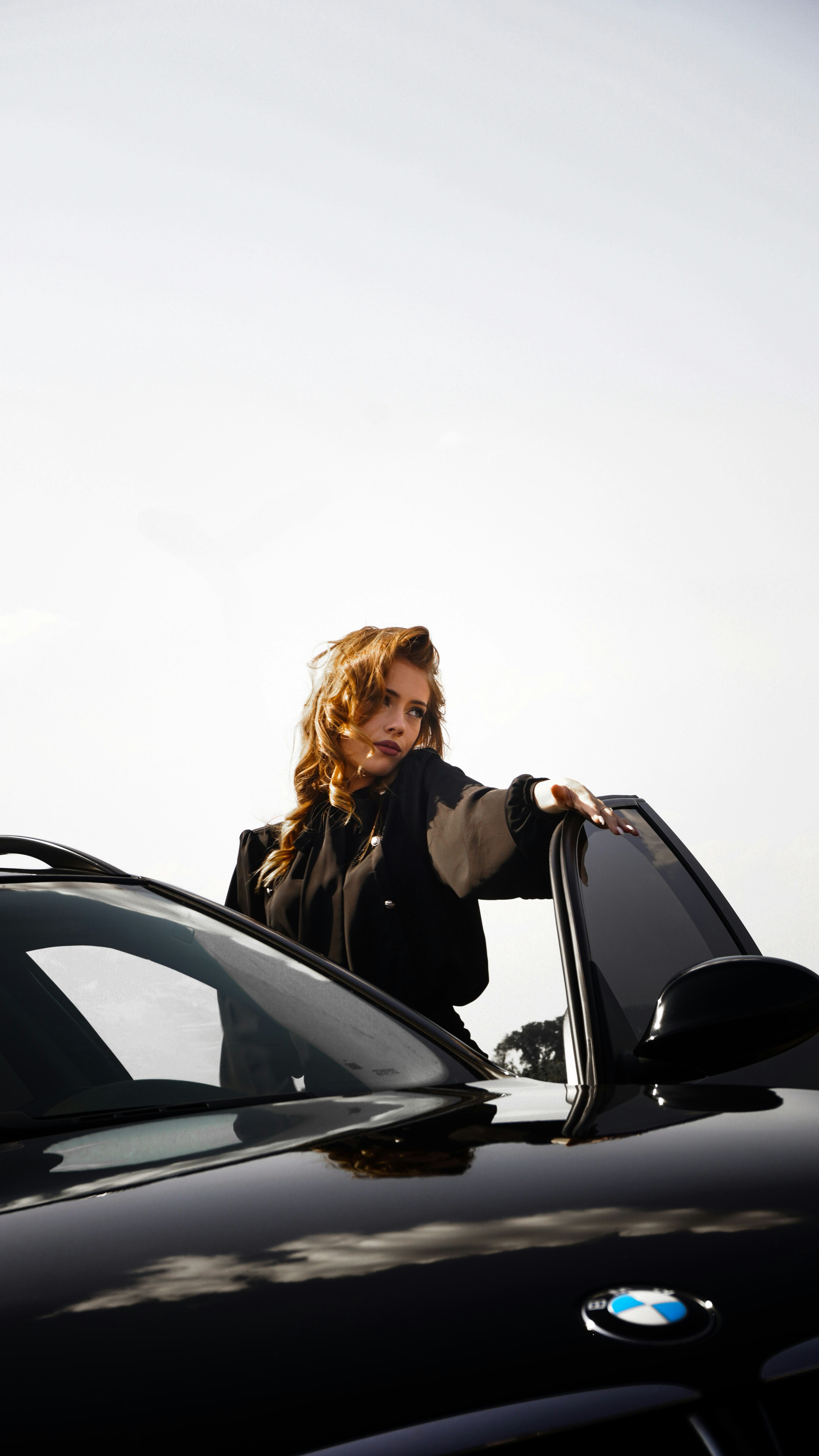 A woman leaning on a car talking on a cell phone
