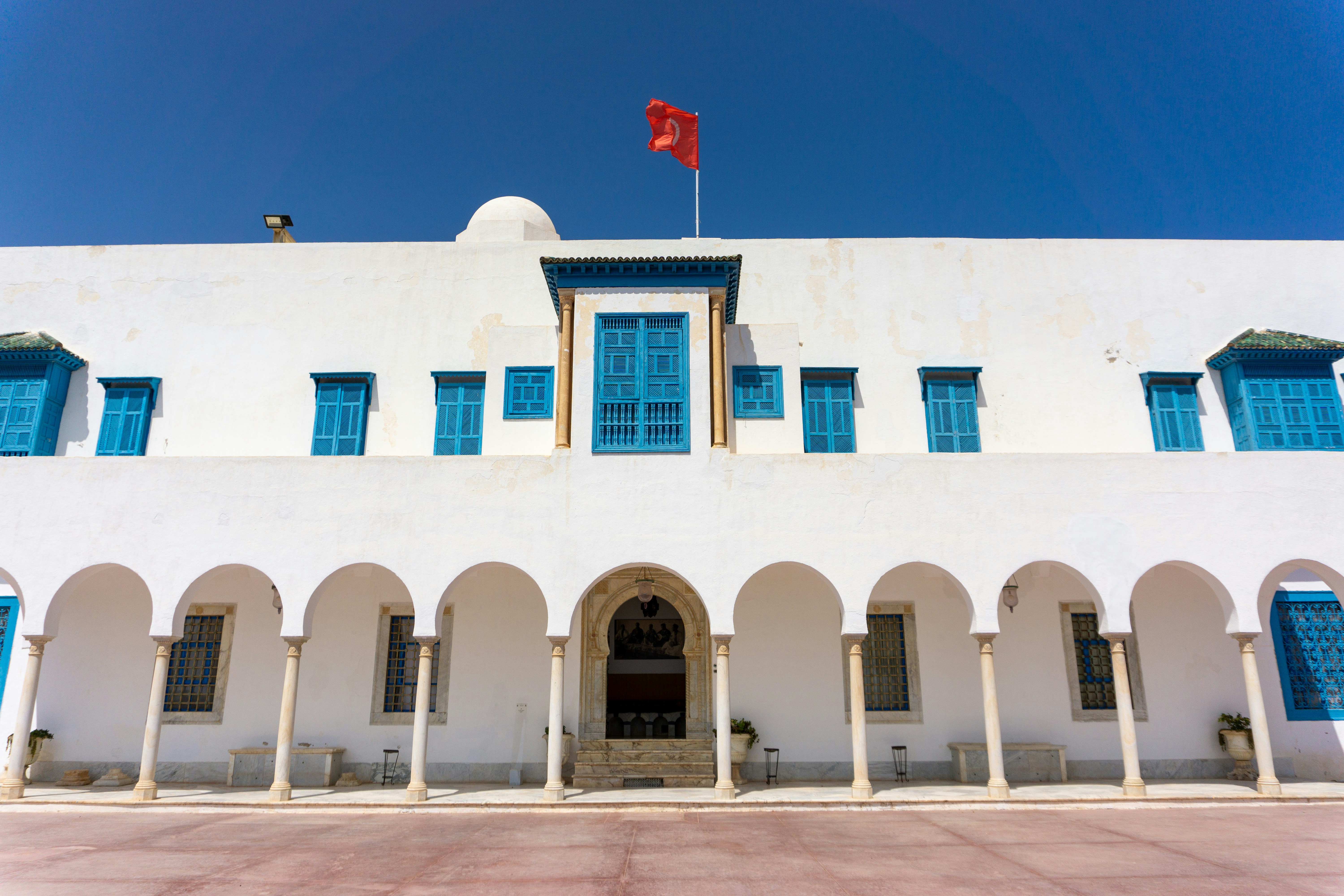 A white building with blue shutters and a flag on top of it