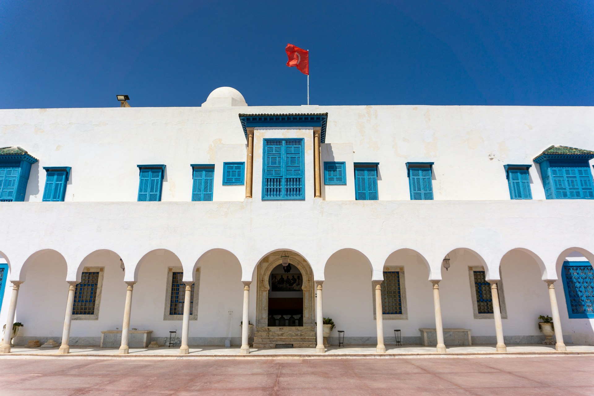 A white building with blue shutters and a flag on top of it