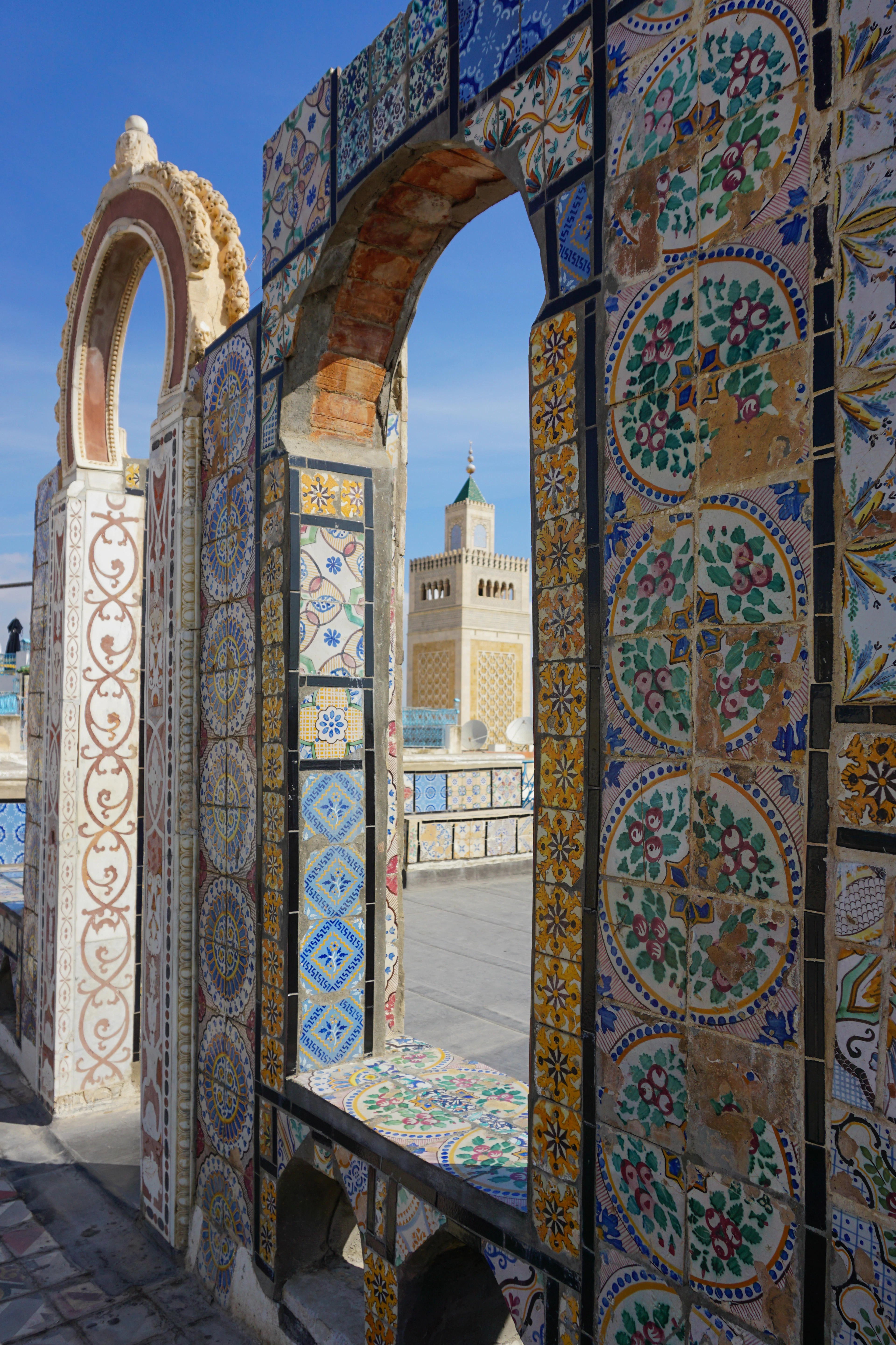 Ornate mosaic-tiled archways frame a view of a distant minaret against a clear blue sky.