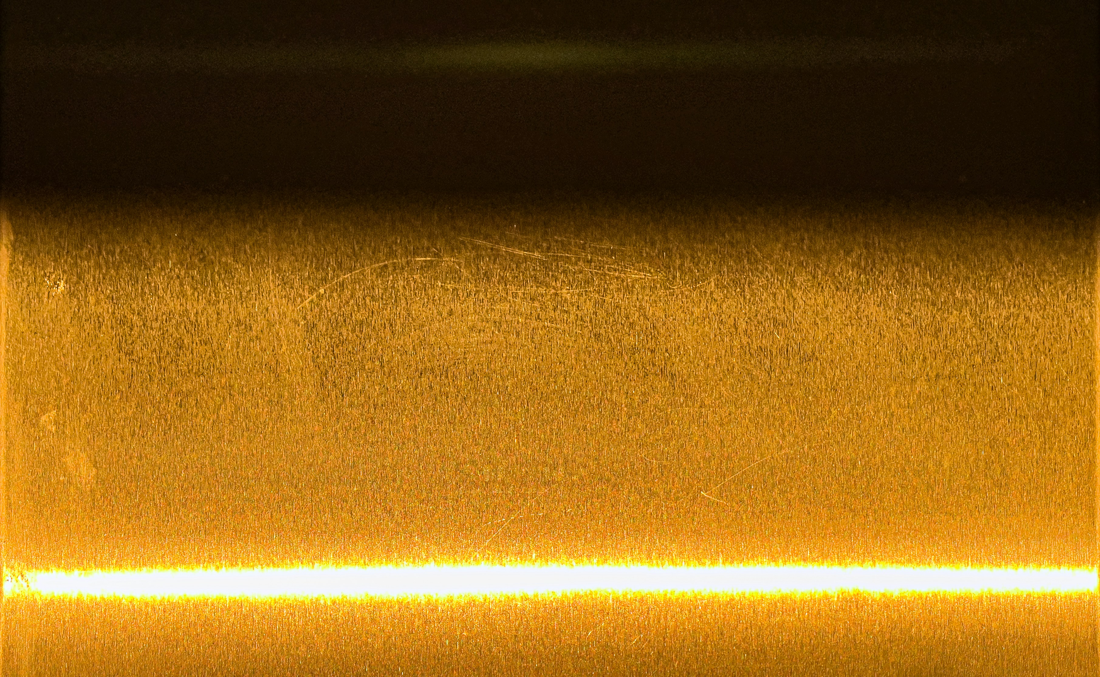 Close-up of shiny metallic surface with reflective texture, warm golden light, smooth polished metal