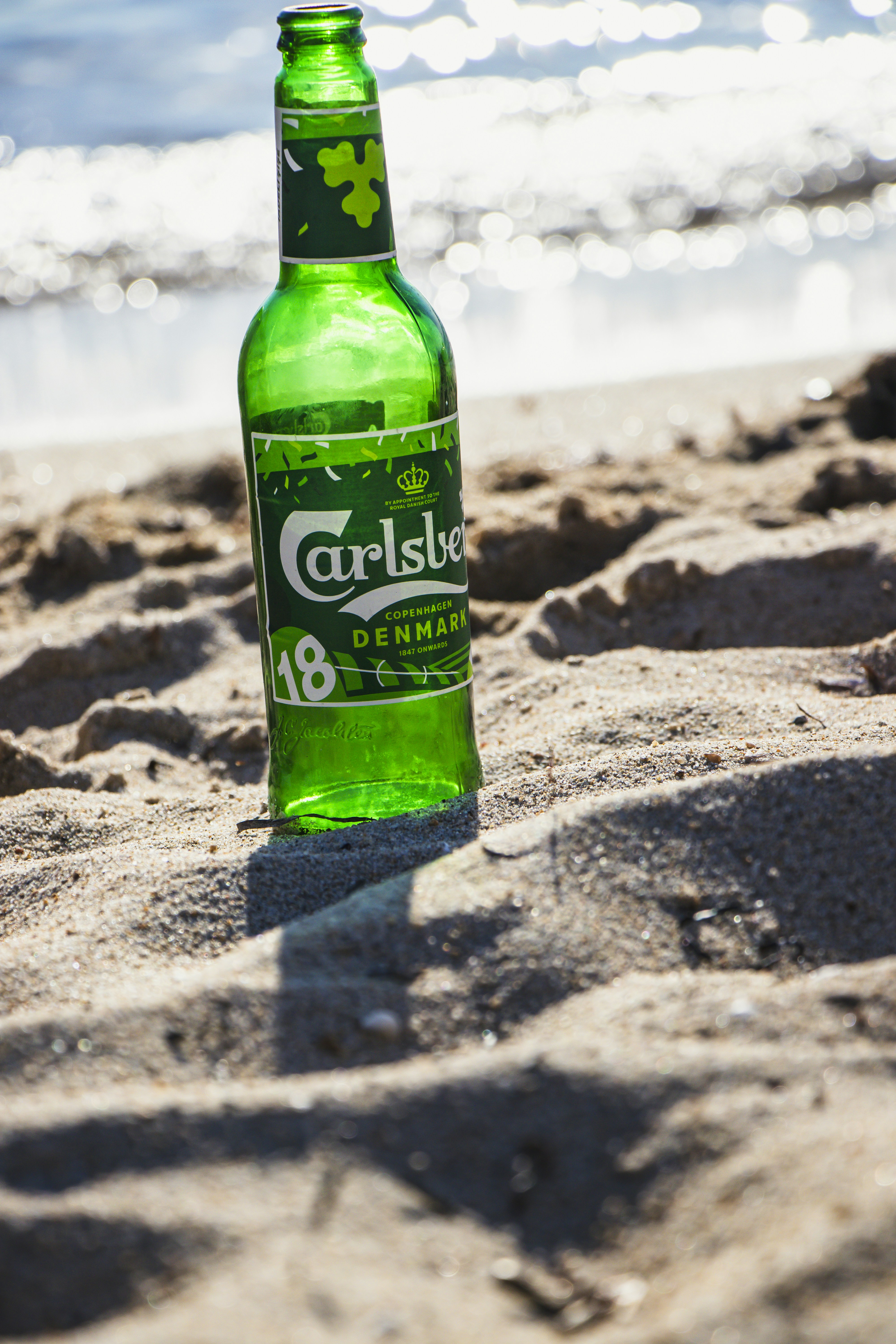 A green bottle sitting on top of a sandy beach